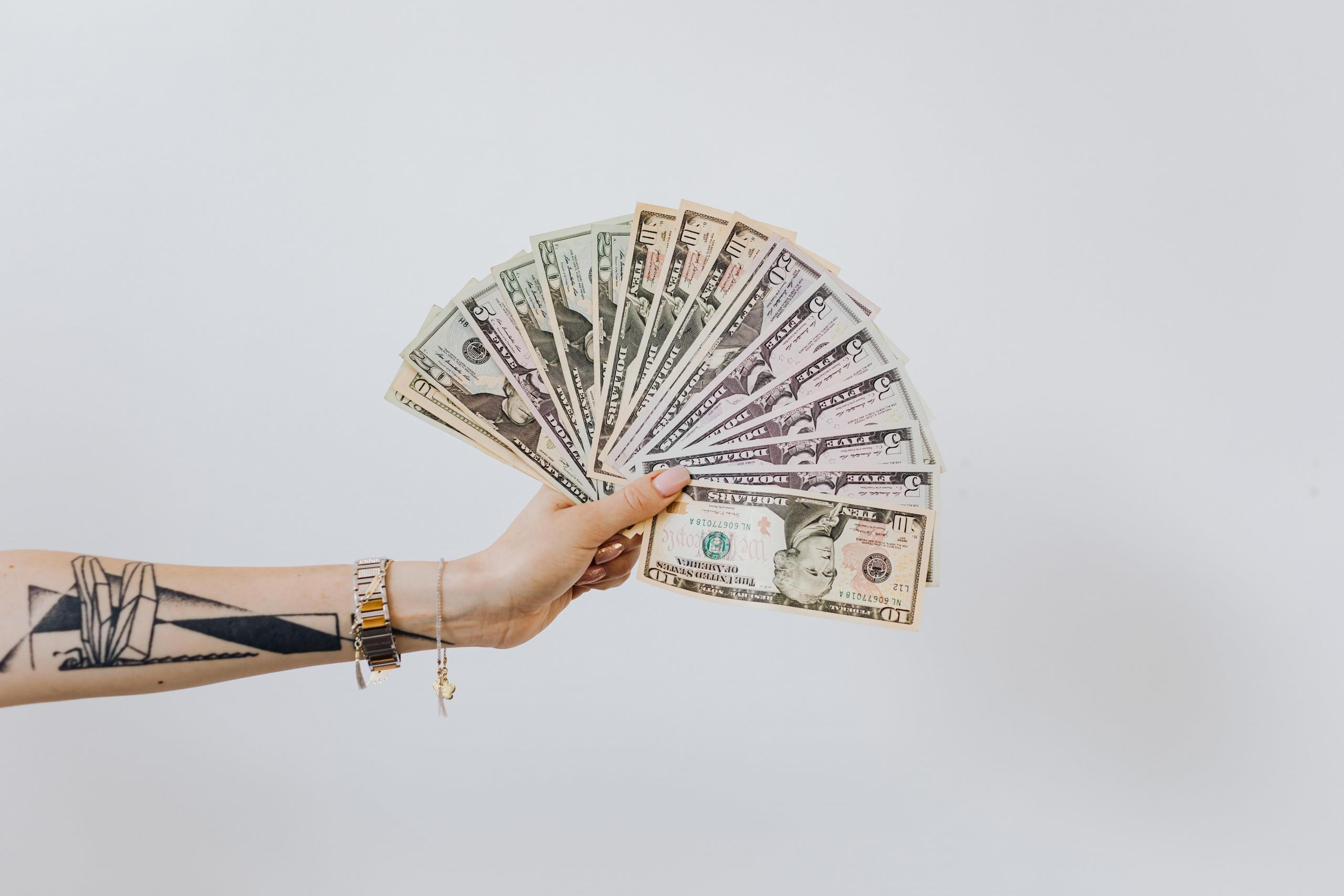 Renkli banknotlar tutan dövmeli el