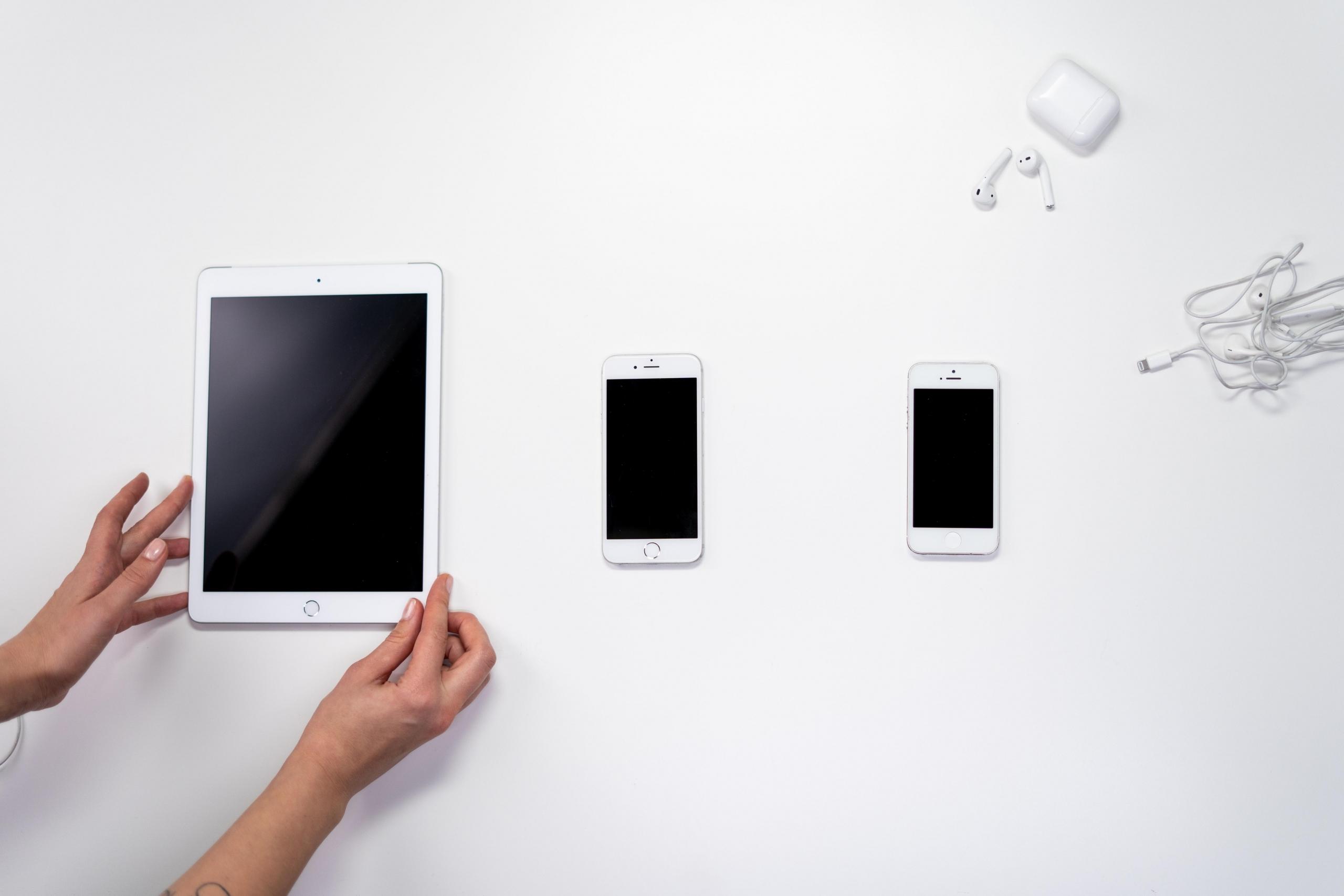 Beyaz masanın üstünde beyaz tablet ve iki telefon