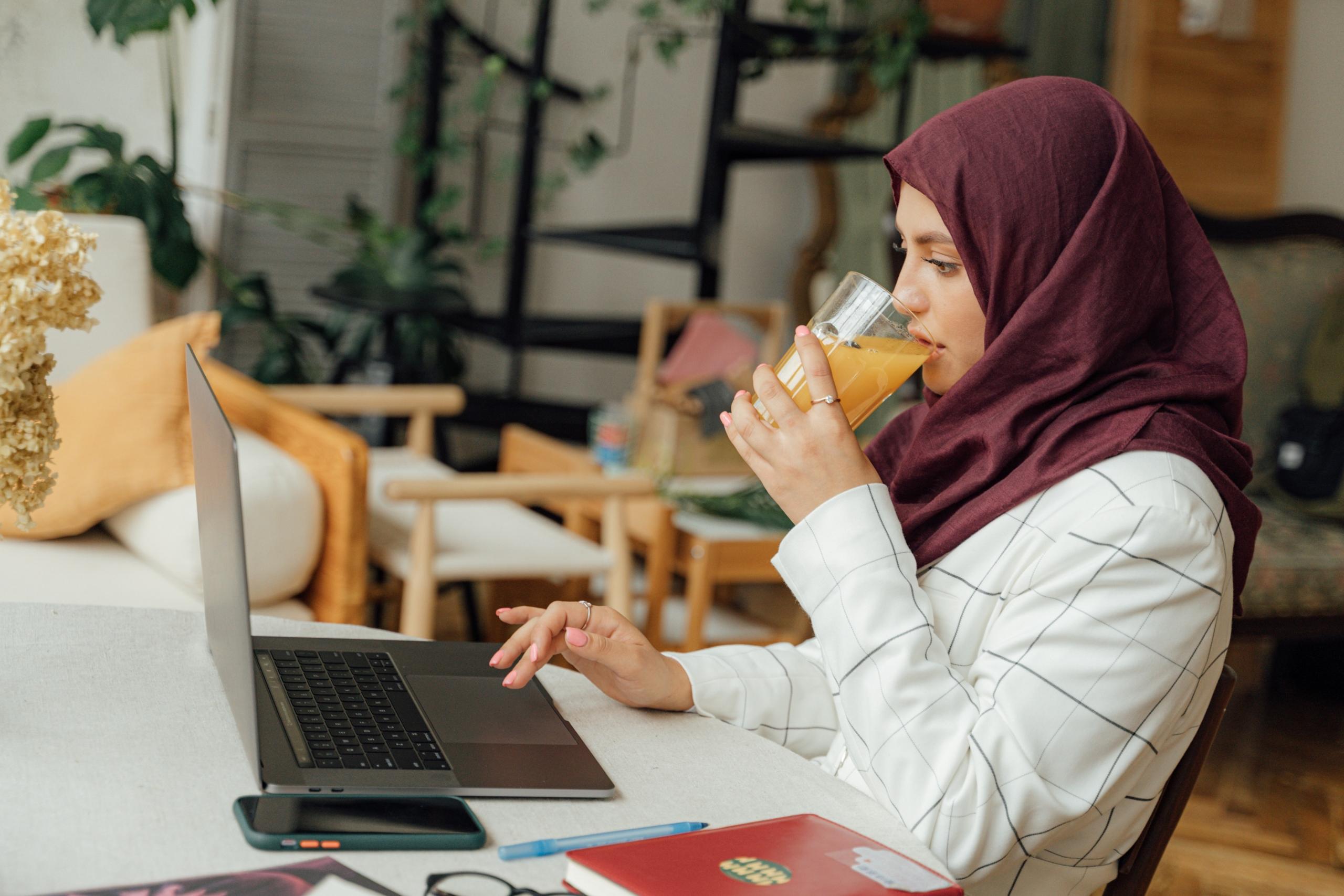 Meyve suyu içerken laptop ile ilgilenen kadın