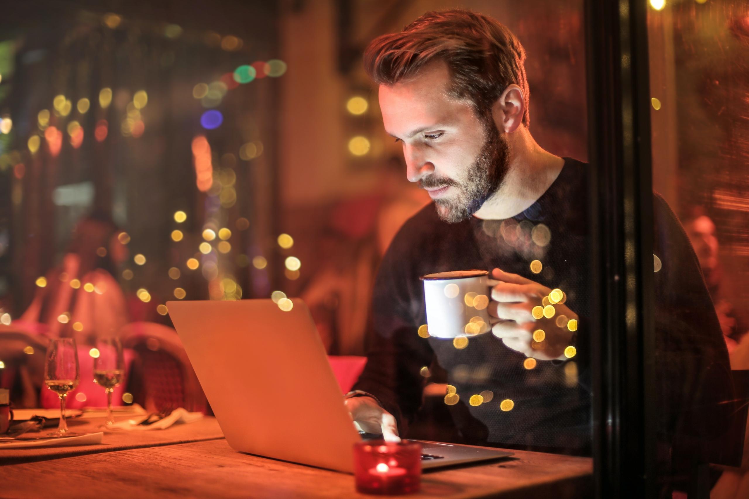 Dışarıda kahve içerken laptopa bakan sakallı adam