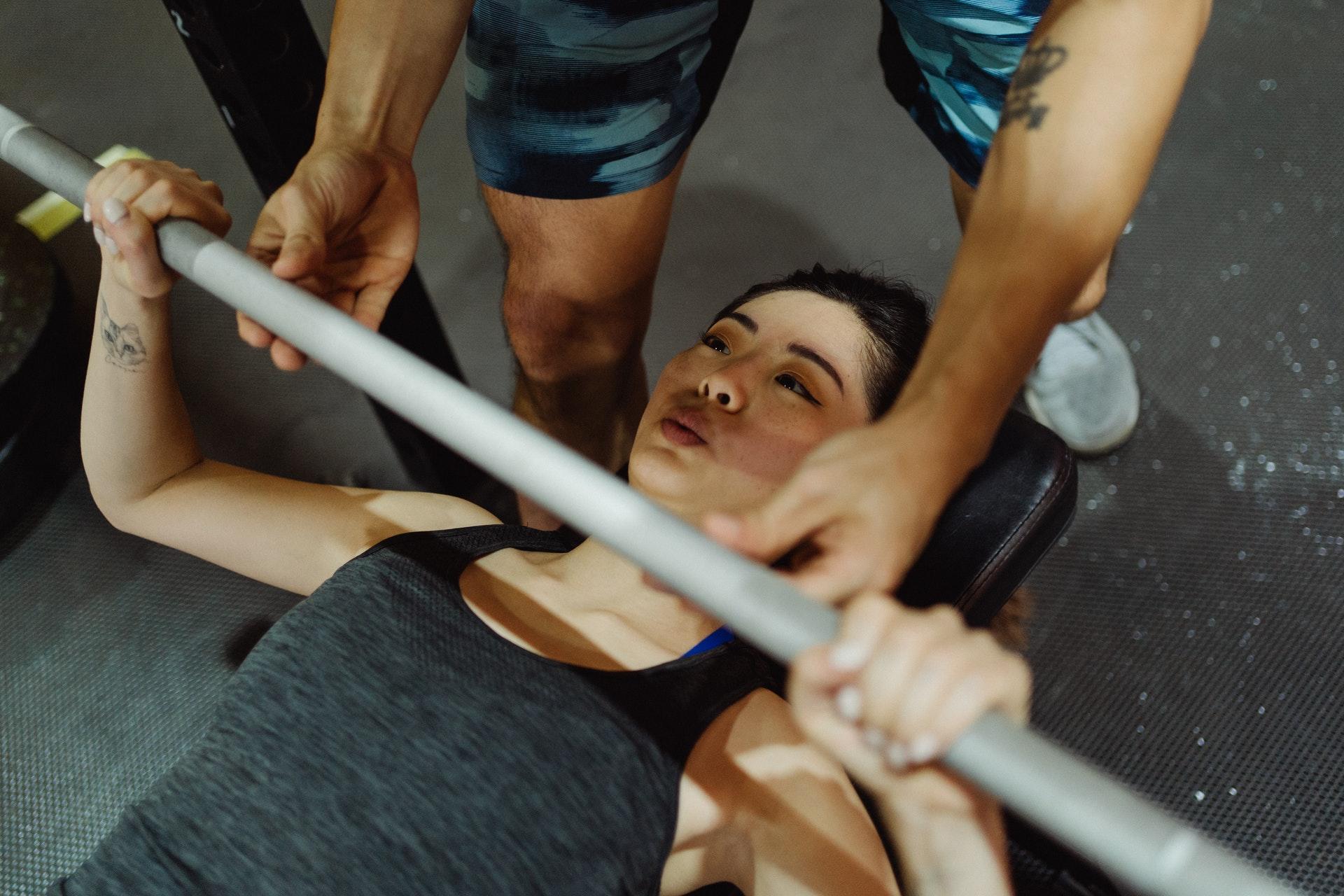 Bench press yapan kadına yardım eden adam