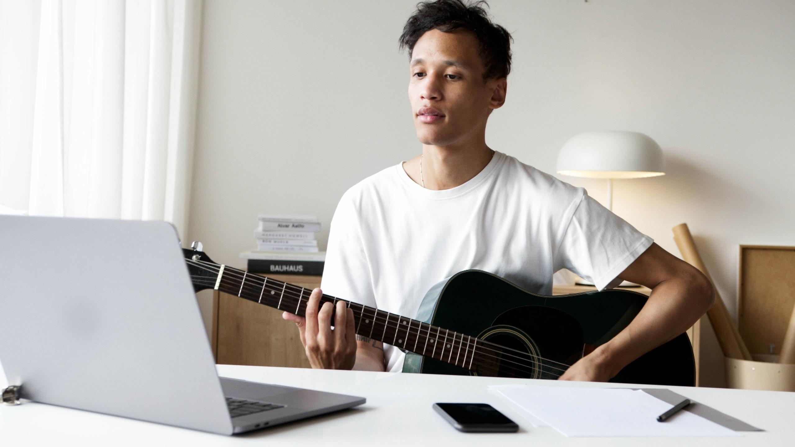 Laptopa karşı gitar çalan beyaz tişörtlü erkek