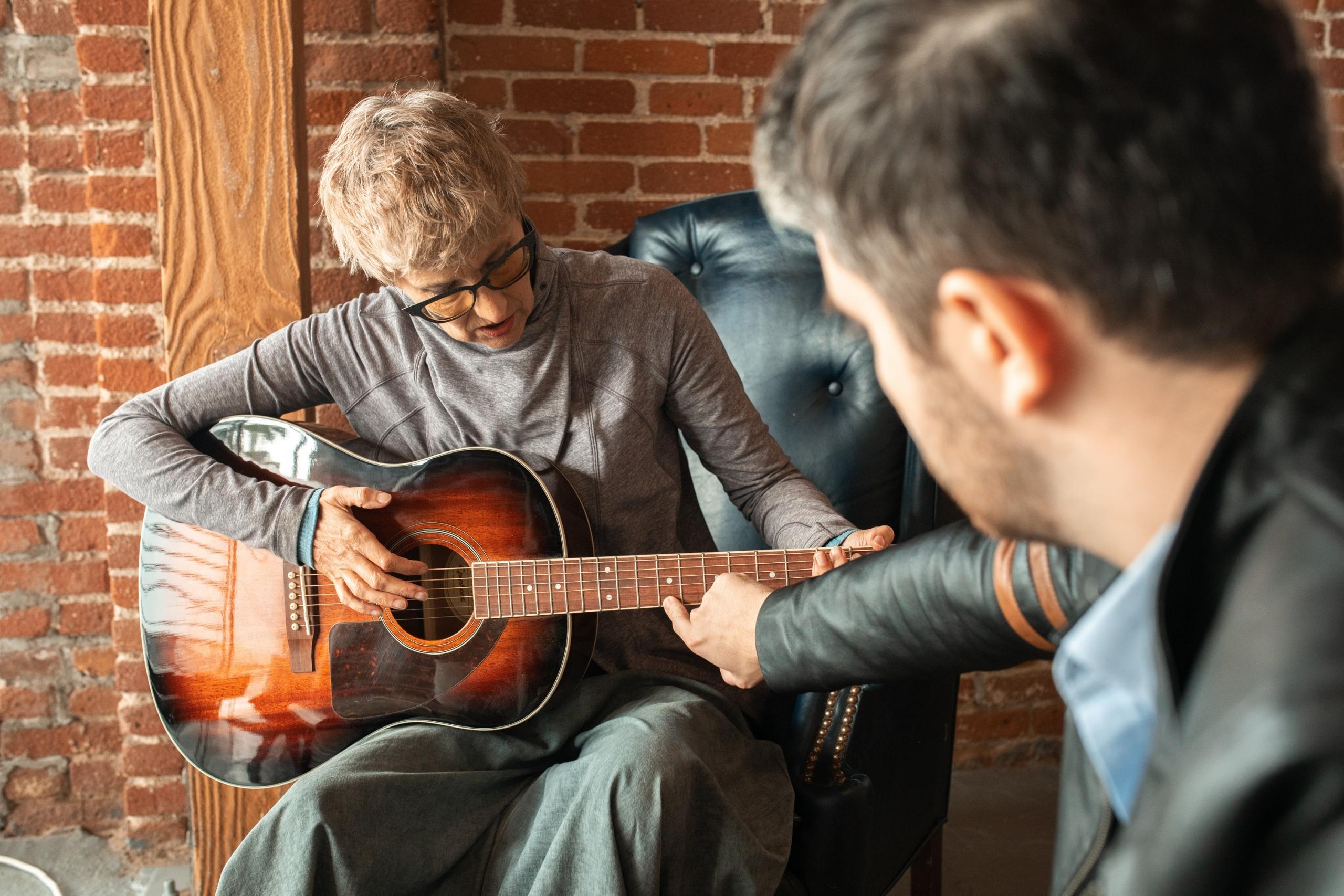 Klasik gitar çalan adamla gitarı işaret eden siyah ceketli adam