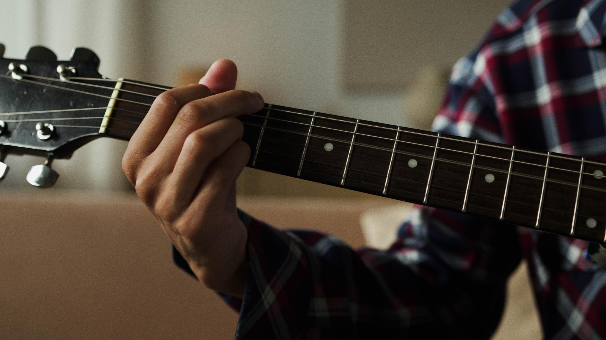 Gitarın perdelerine parmaklarını koymuş kareli gömlekli adam