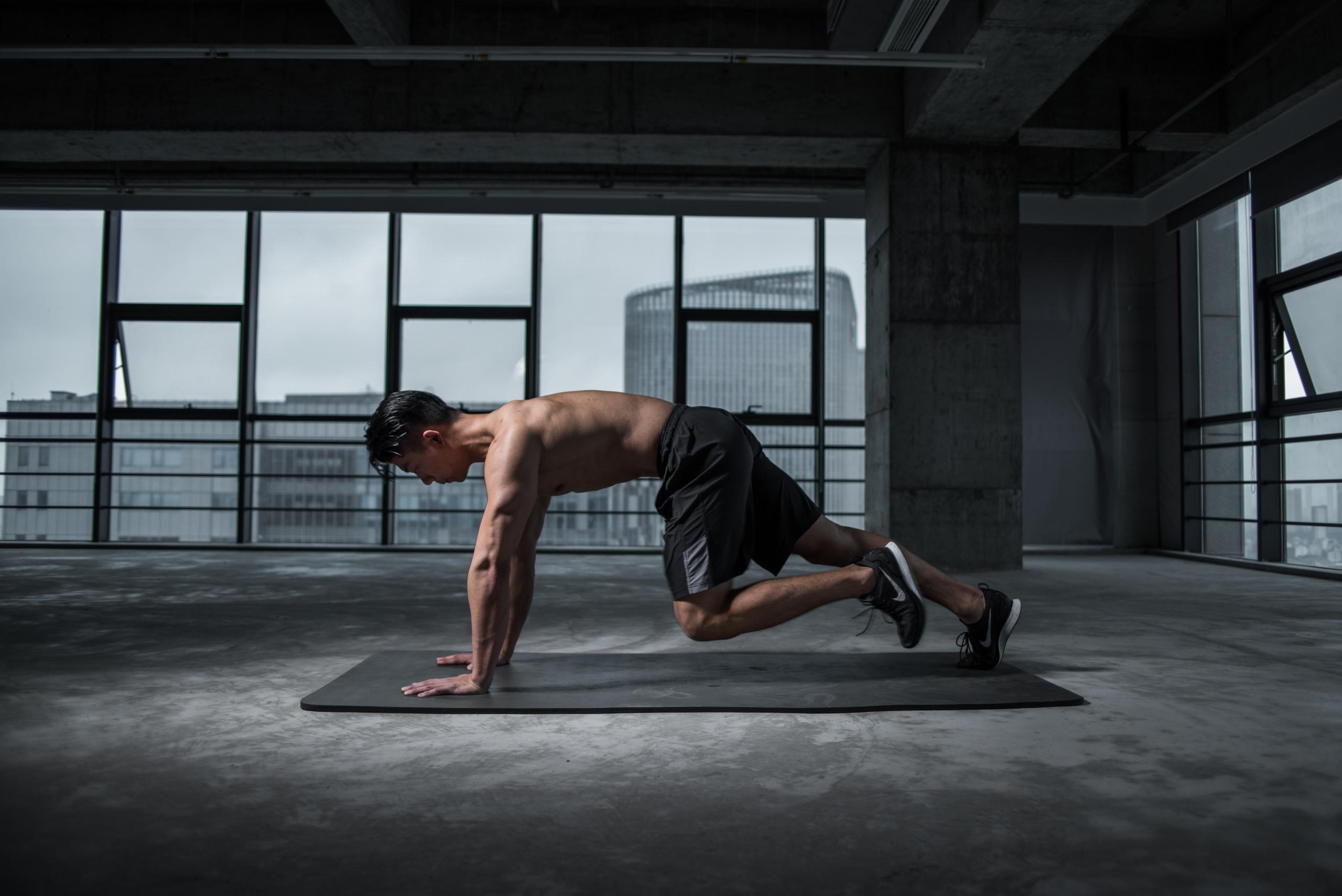 Büyük pencereli boş odada matın üstünde spor yapan üstsüz adam