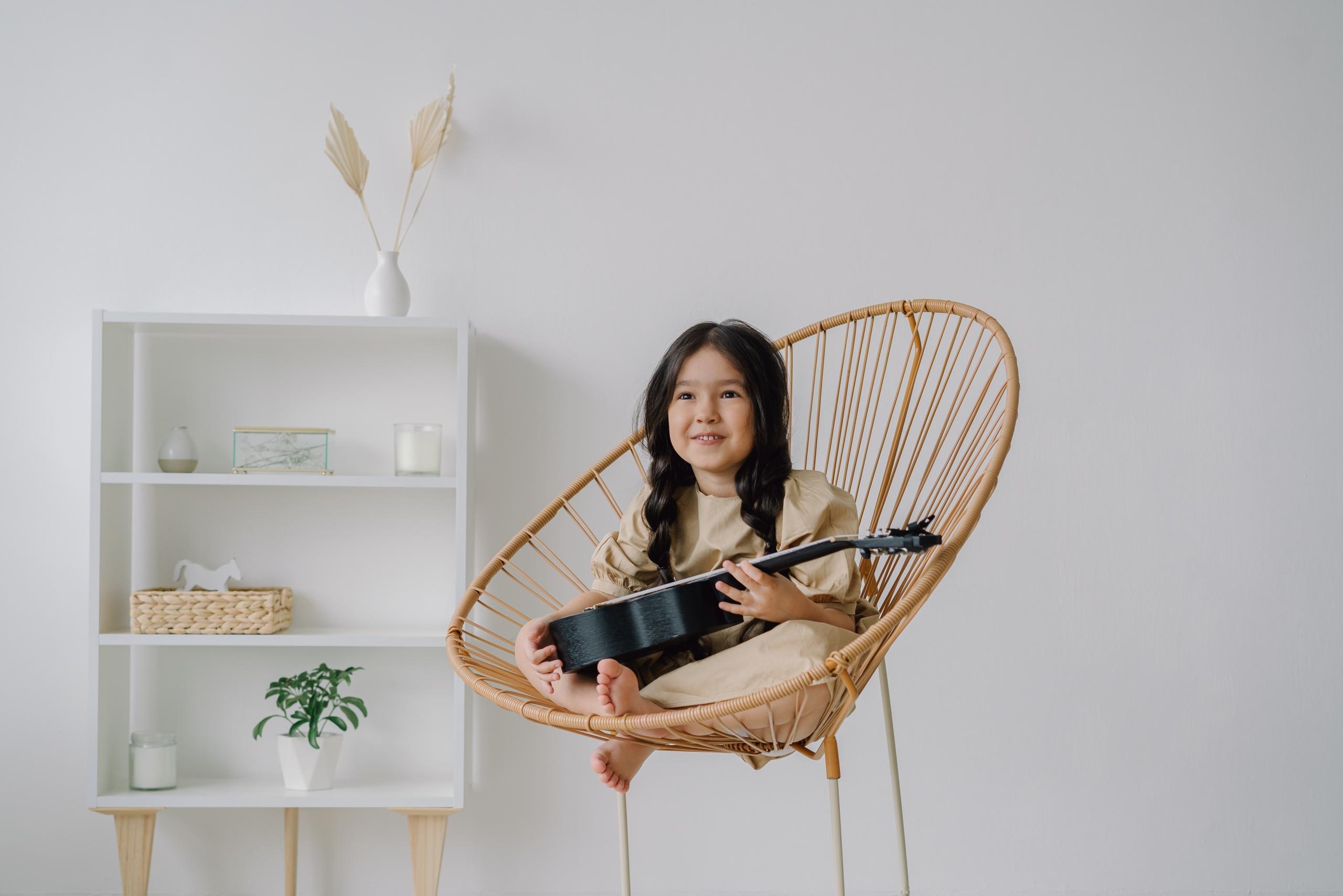 Sandalyede bağdaş kuran elinde ukulele tutan küçük kız çocuğu