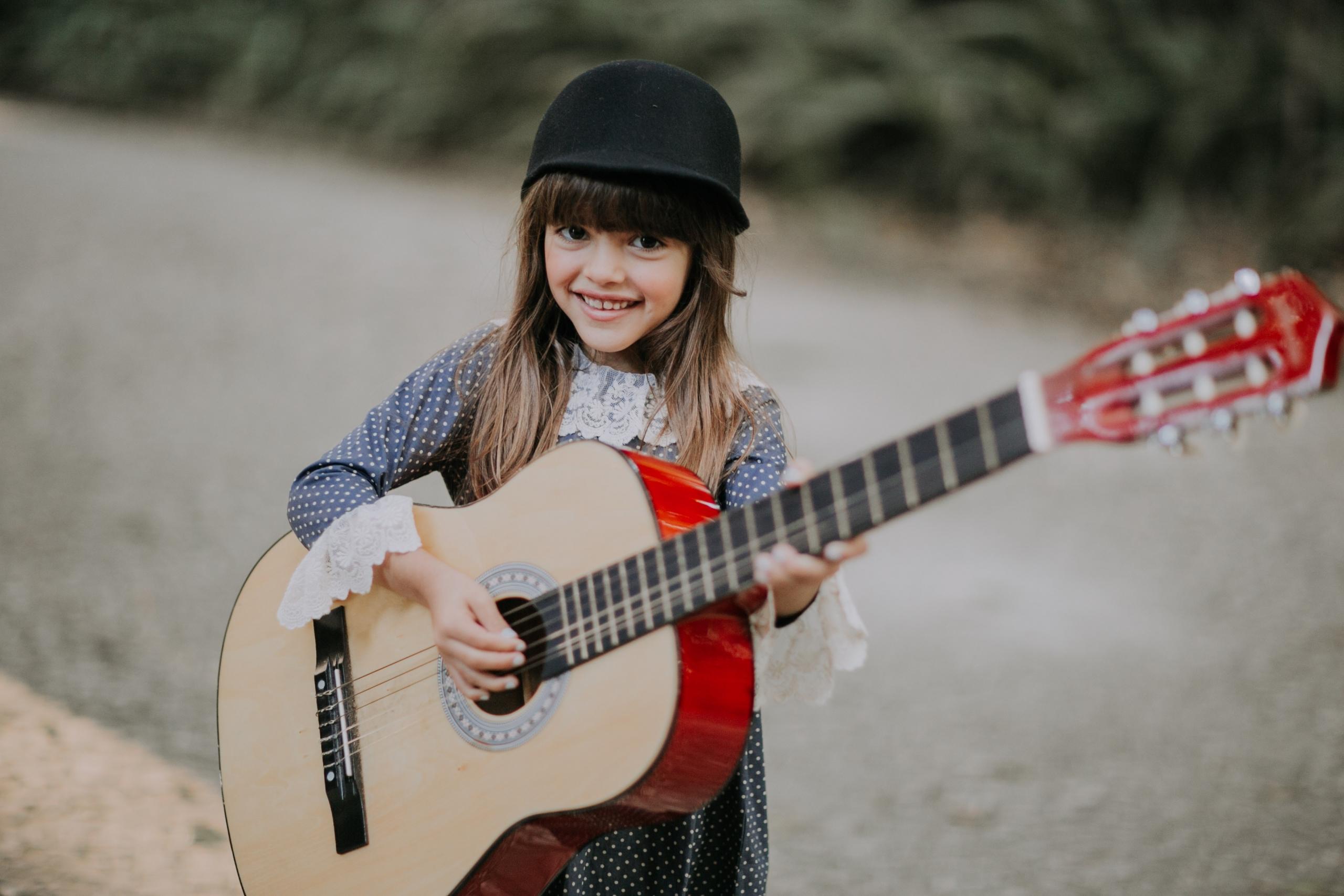 Gitar çalan şapkalı küçük kız çocuğu