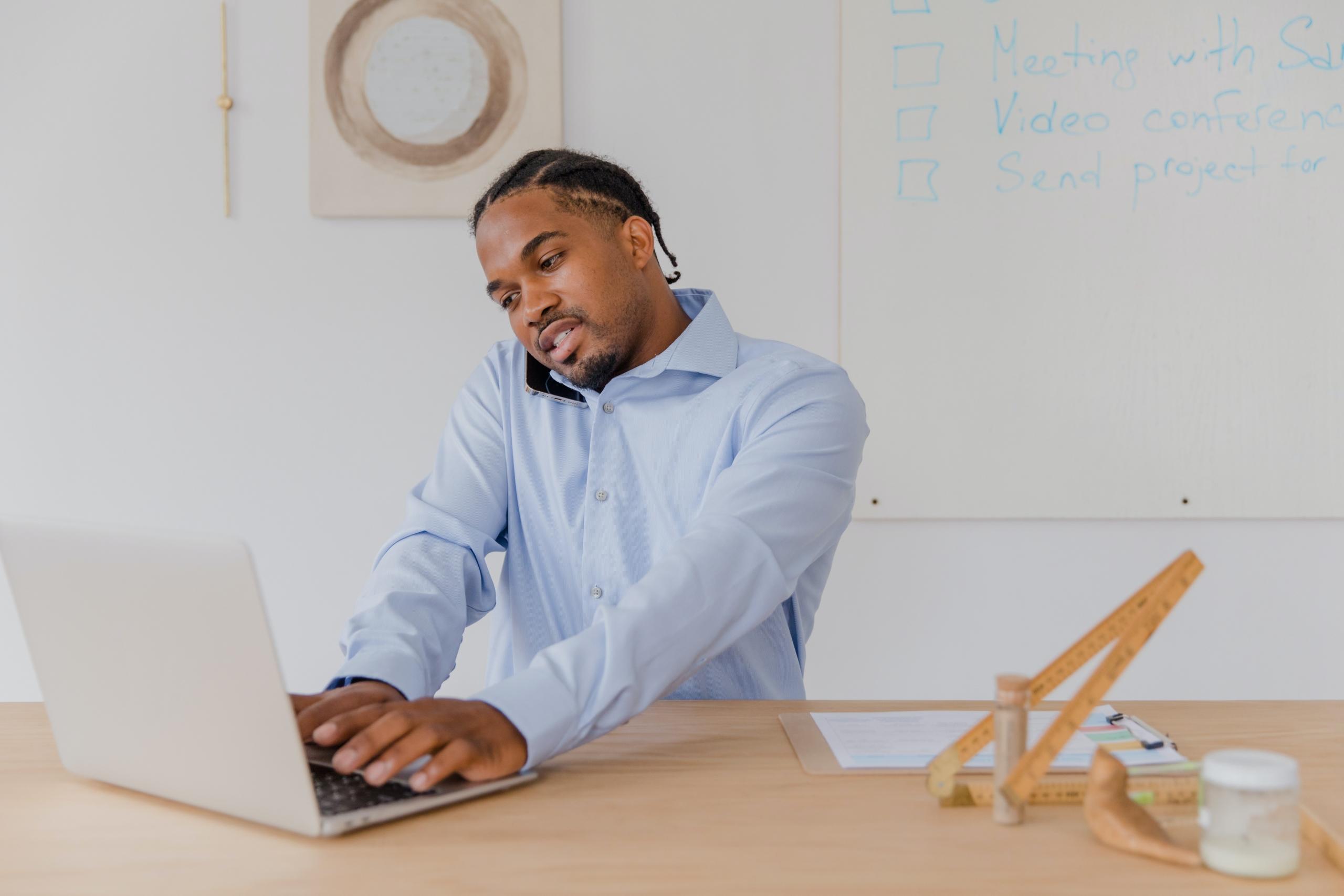 Telefonda konuşurken laptopta bir şeyler yazan adam