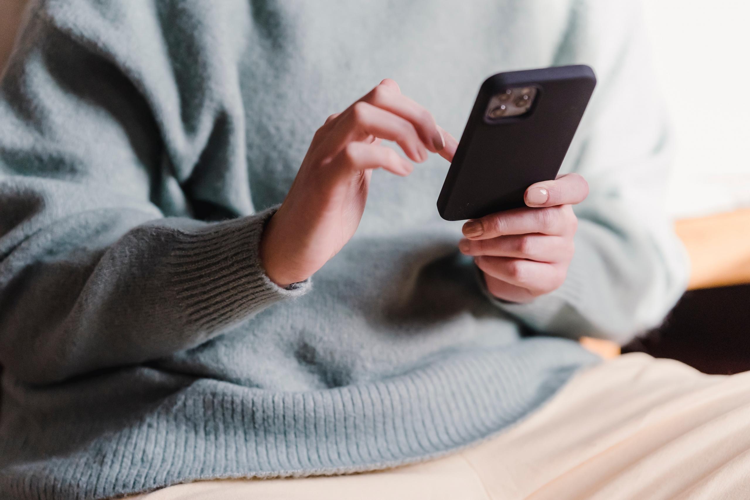 Telefonunda bir şeylere bakan mavi kazaklı adam