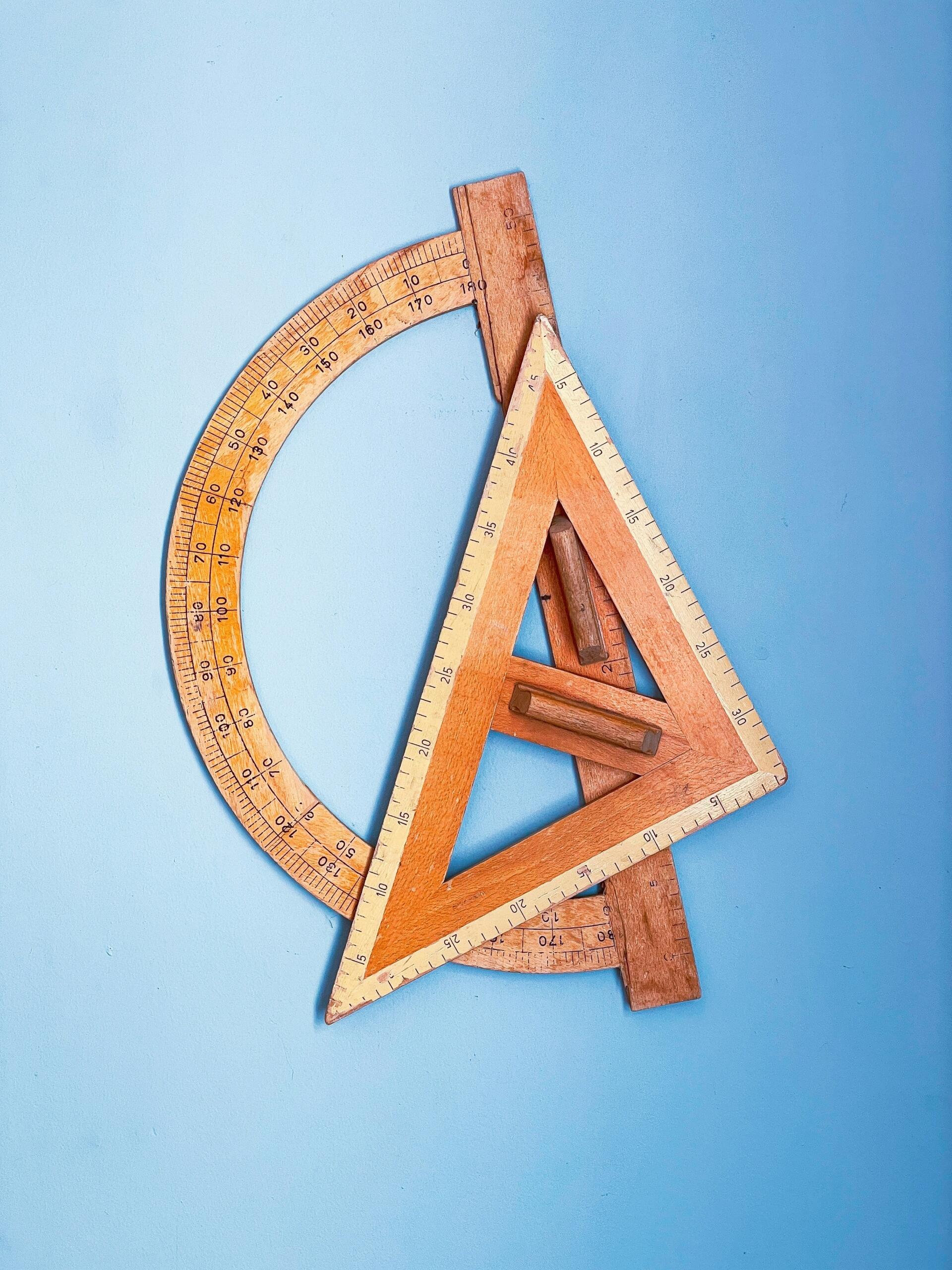 Mavi bir zemin üzerinde, ahşap gönye ve açıölçer gibi geometri araçları üst üste duruyor.