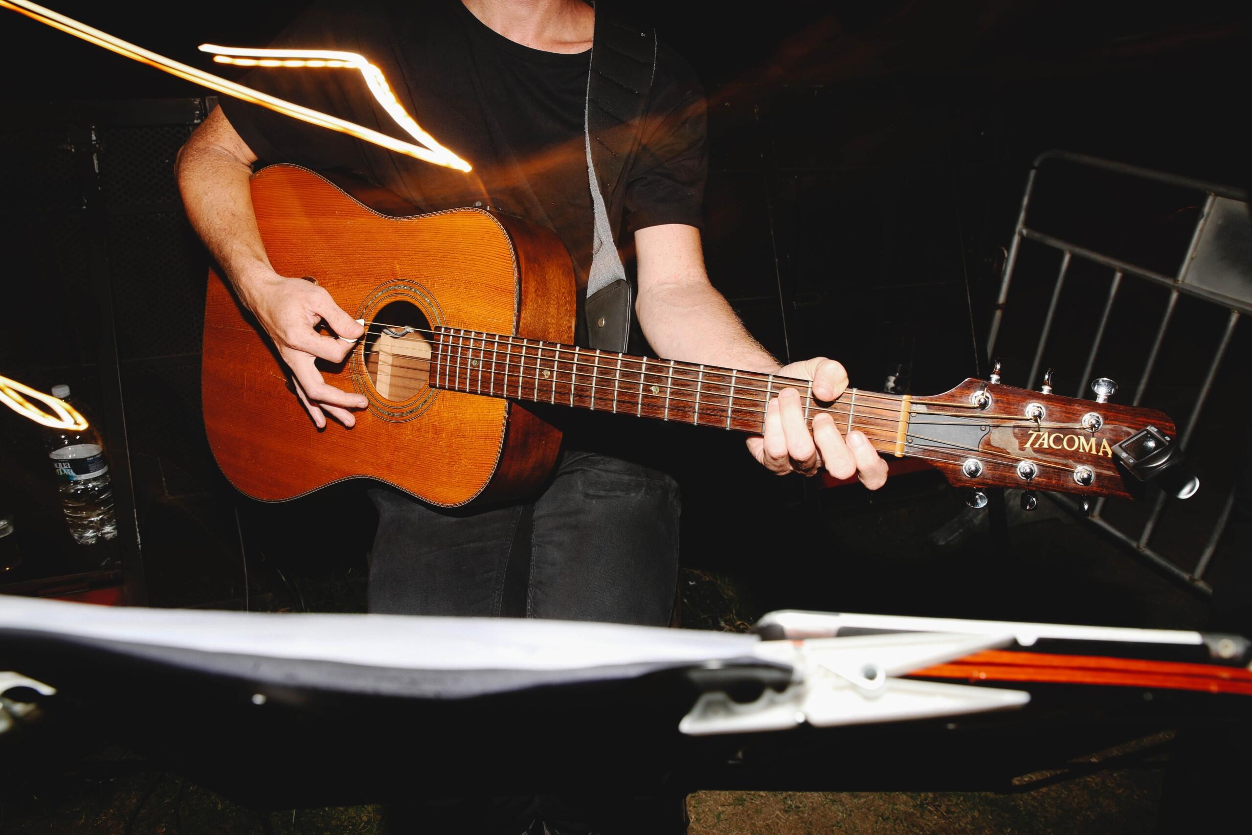 Bir kişi, karanlık bir ortamda ahşap gövdeli akustik gitar çalıyor.