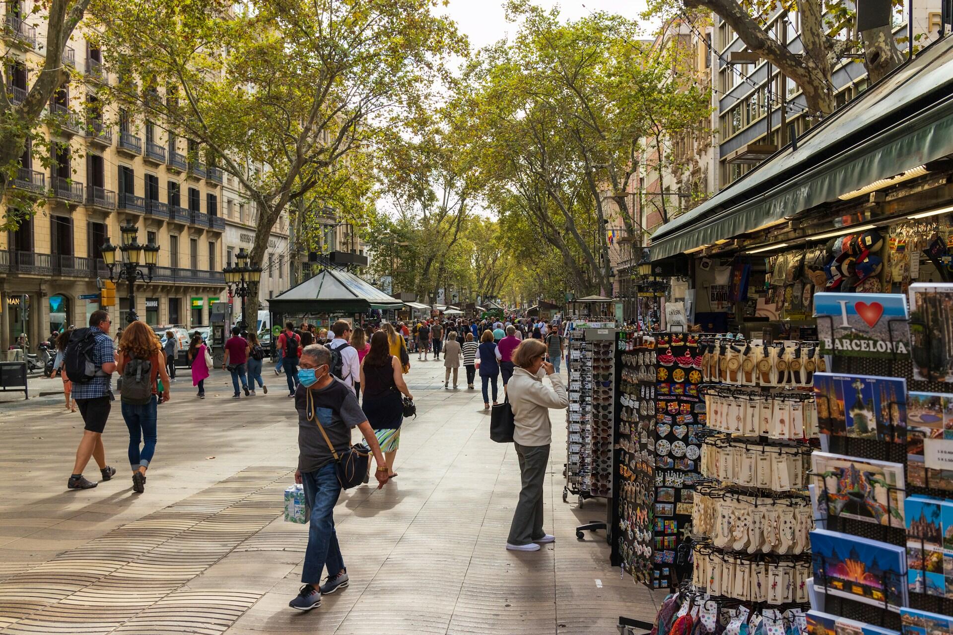 Barselona’nın ünlü La Rambla caddesinde yürüyen insanlar ve hediyelik eşya tezgahlarıyla canlı şehir atmosferi