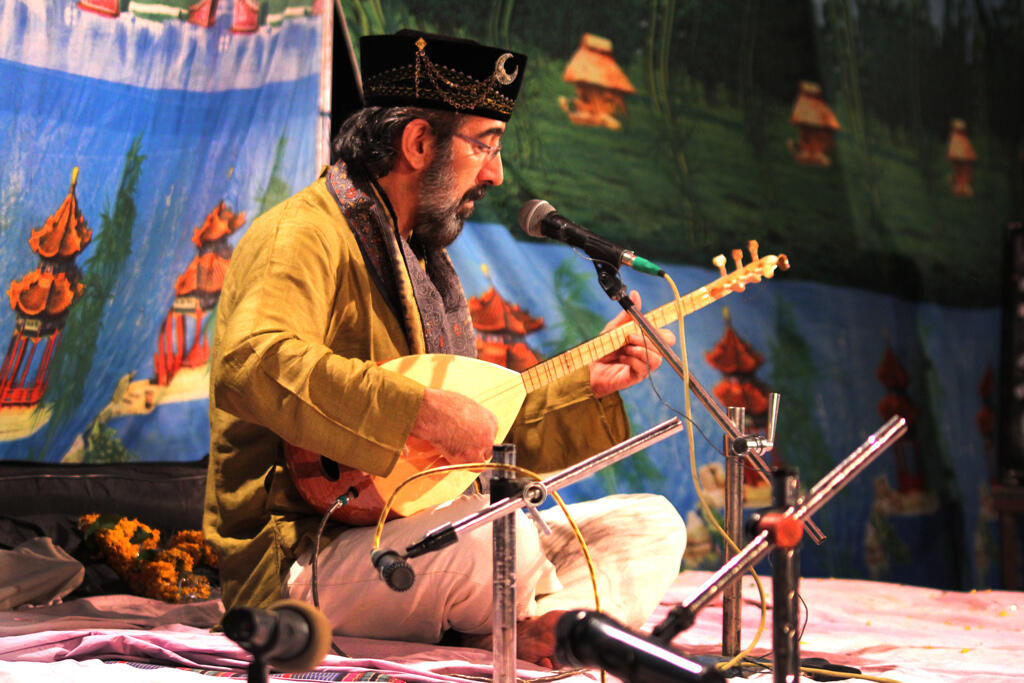 yere bağdaş kurmuş şekilde oturarak bağlama çalan modern bir halk ozanı