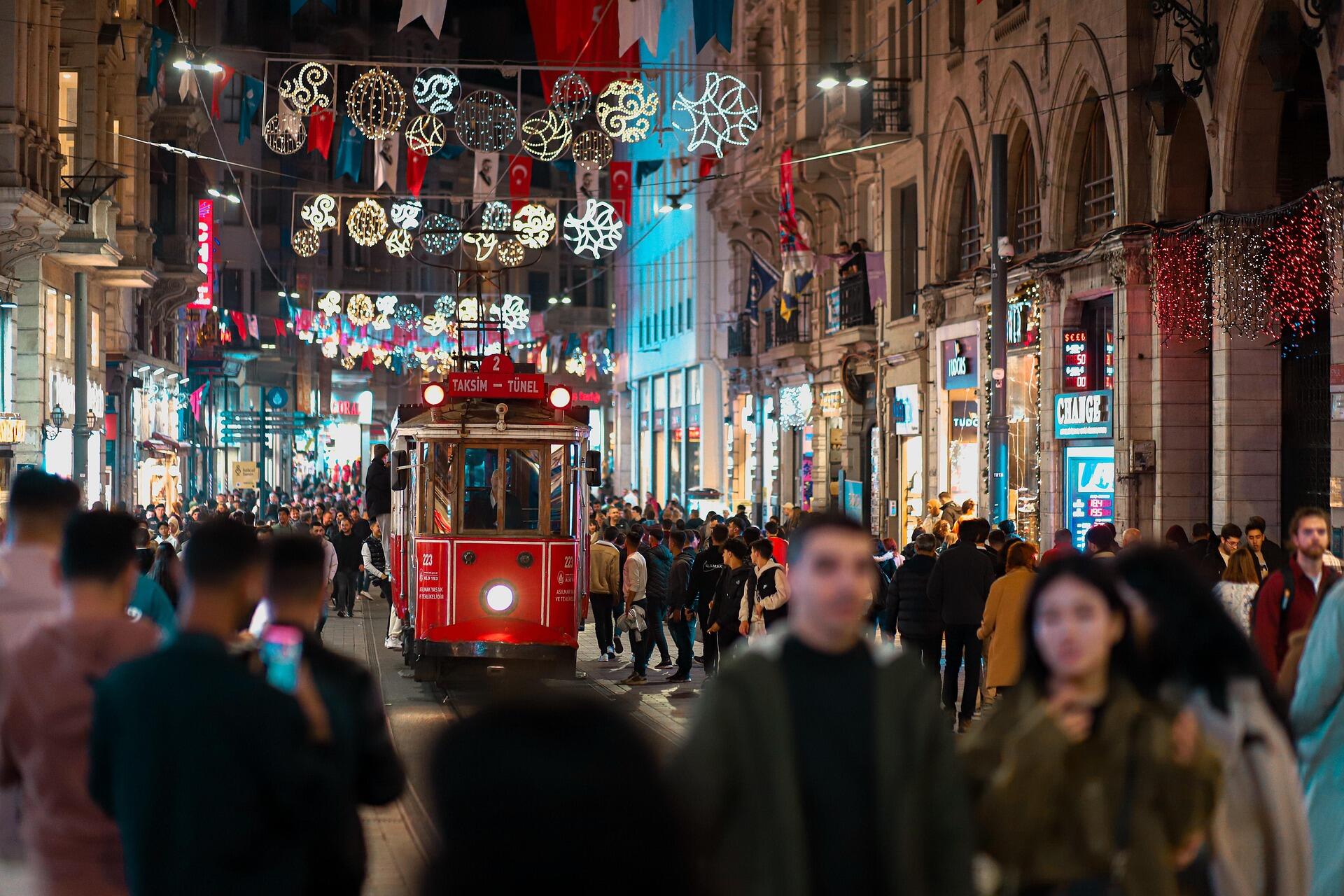 İstanbul’un ünlü İstiklal Caddesi’nde gece vakti ilerleyen nostaljik kırmızı tramvay, etrafı ışıklarla süslü dükkânlar ve kalabalık insanlarla çevrili.