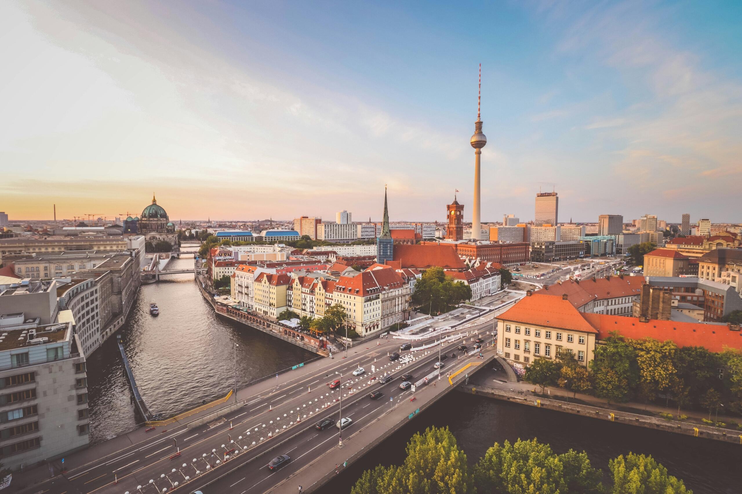 Berlin şehir merkezinin, Spree Nehri, köprüler, tarihi yapılar ve ikonik Televizyon Kulesi (Fernsehturm) eşliğinde gün batımında panoramik bir görünümünü gösteriyor.