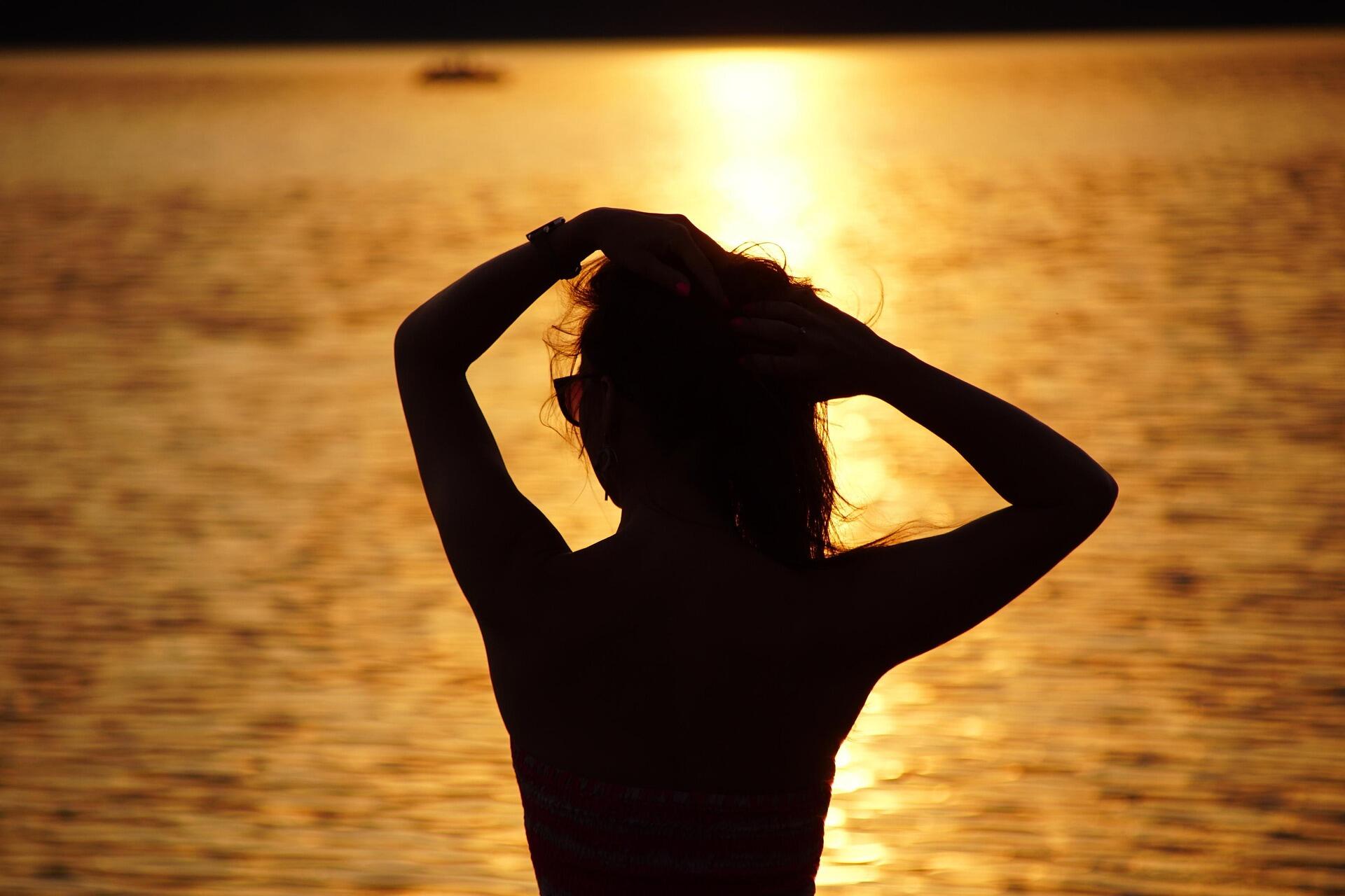 Gün batımında denize karşı duran ve pozitif enerji veren şarkılar dinleyerek rahatlayan bir kadın silüeti.