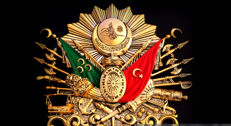 Osmanlı İmparatorluğu’nun armasını gösteren, ortasında Osmanlı tuğrası bulunan ve etrafında sancaklar, silahlar ve devlet sembollerinin yer aldığı tarihi arma illüstrasyonu.