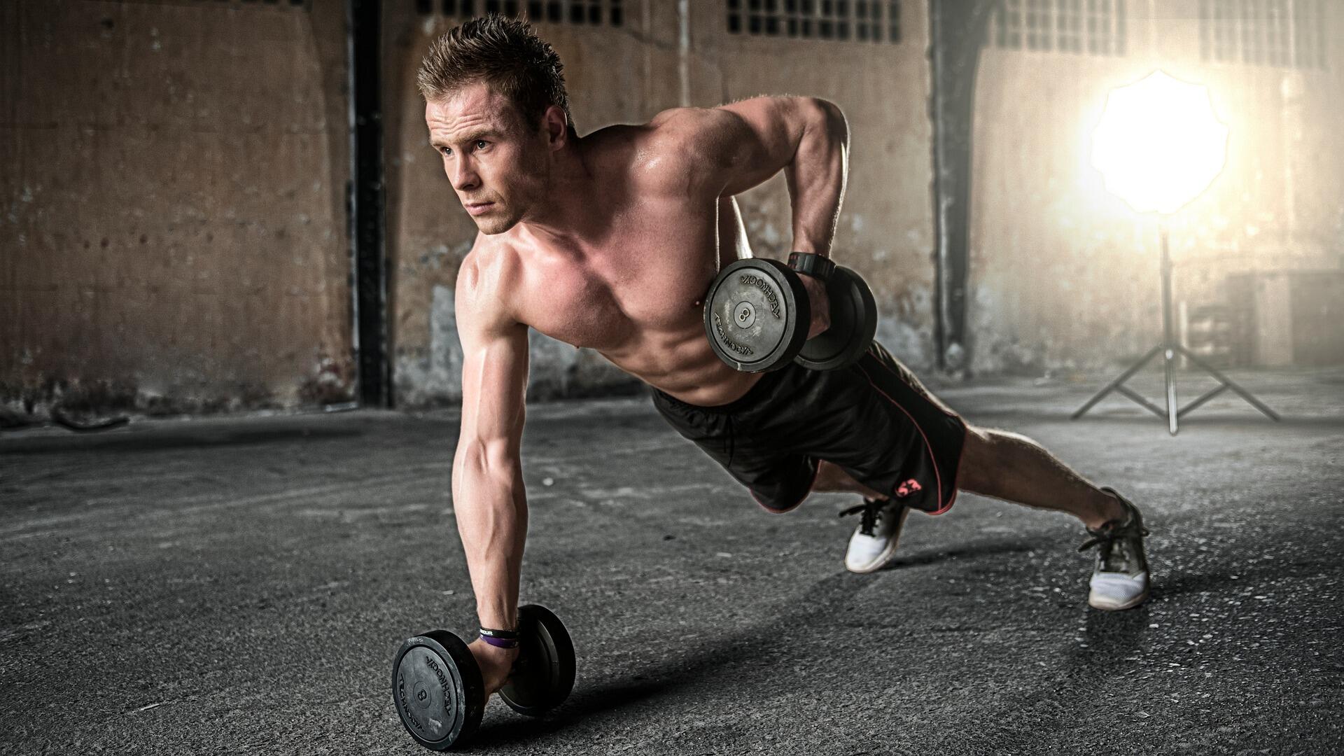 Push up pozisyonunda dumbell çekiş yapan bir atlet