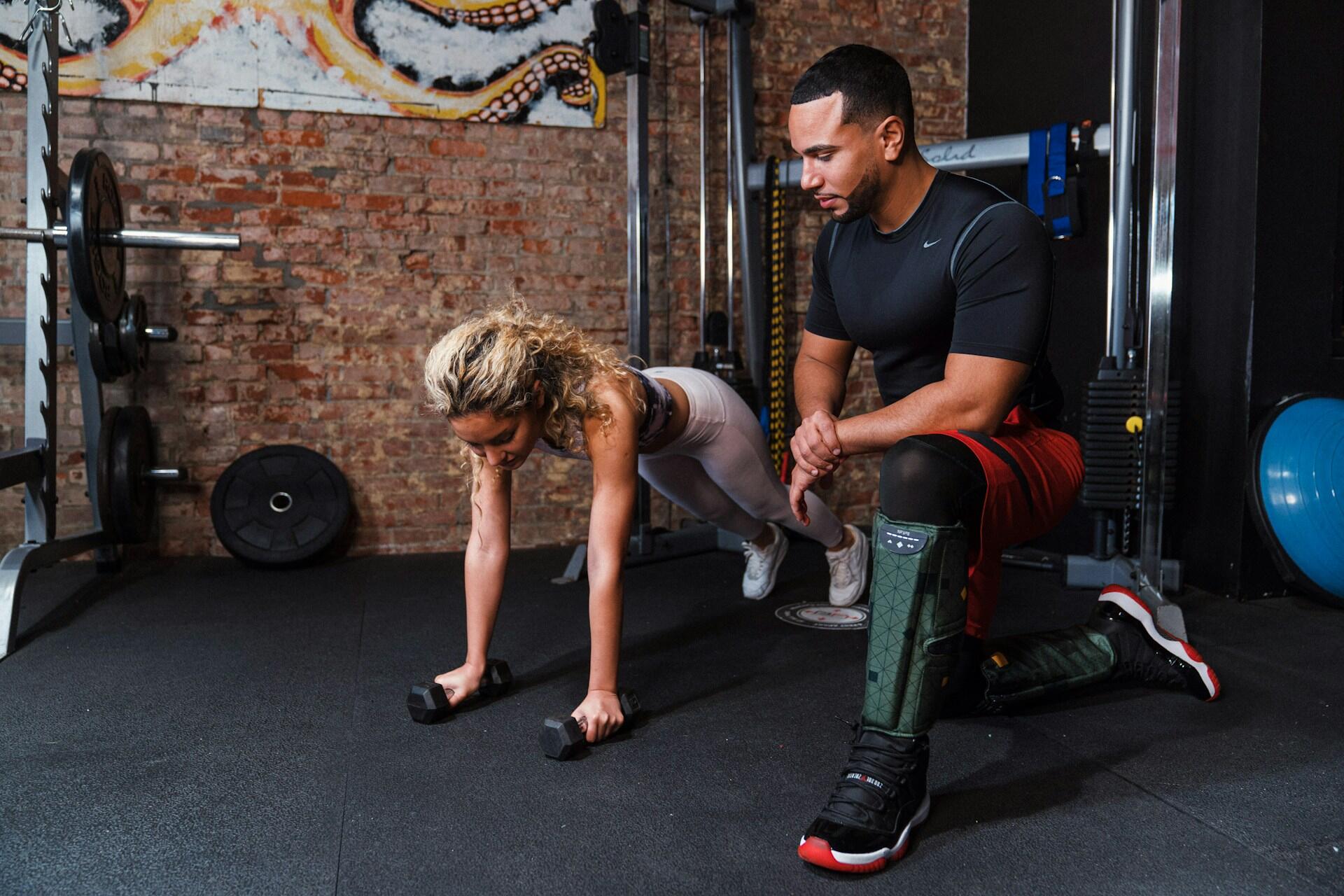 Spor salonunda plank yapan bir kadını izleyen ve rehberlik eden erkek personal trainer