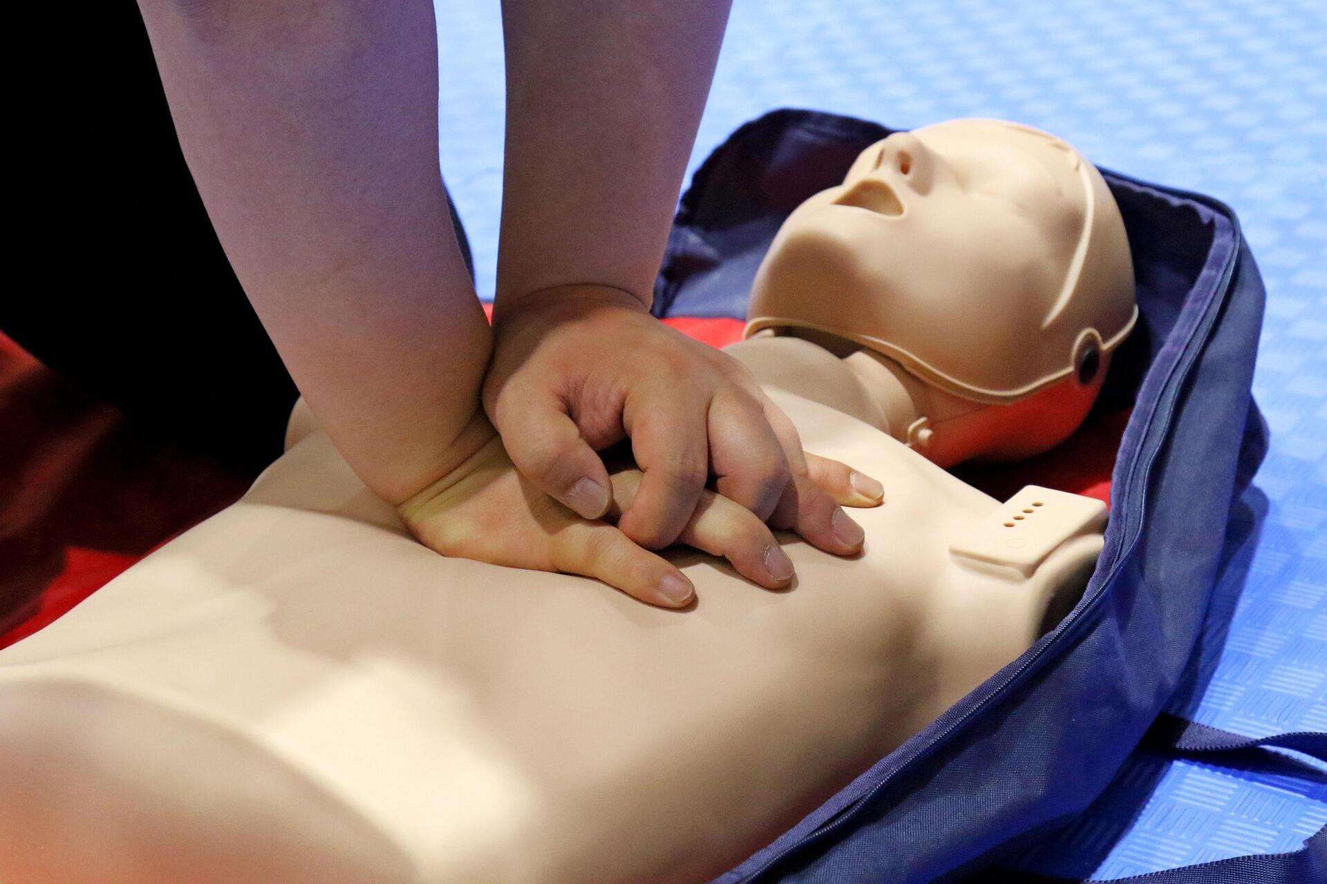İlkyardım maketi üzerinde göğüs basısı yöntemiyle CPR (kalp masajı) uygulaması eğitimi veren bir kişinin elleri yakından görülüyor.