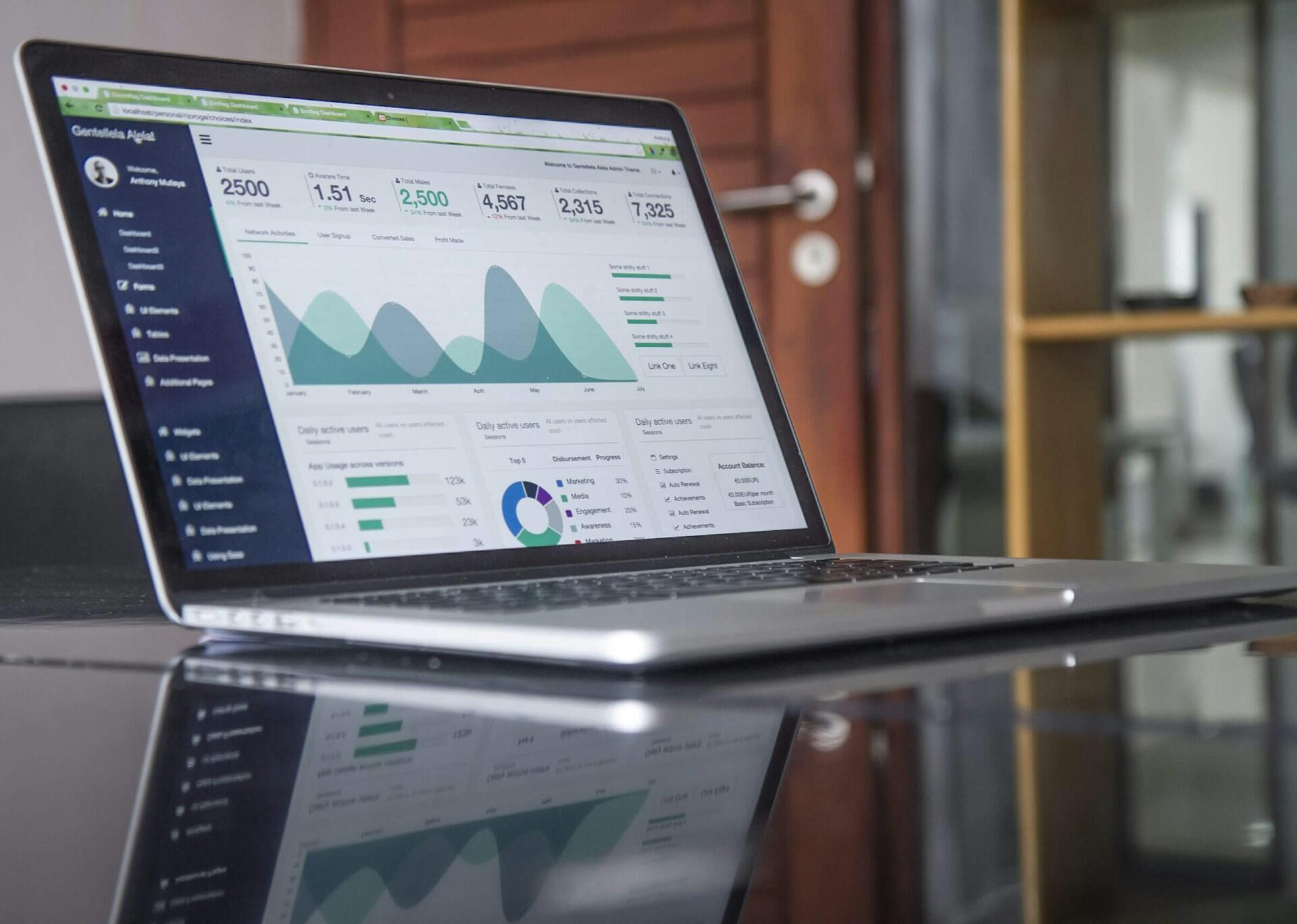 Siyah bir masa üzerinde duran dizüstü bilgisayar ekranında veri analizi, grafikler ve istatistiksel metrikleri gösteren bir yönetim paneli (dashboard).