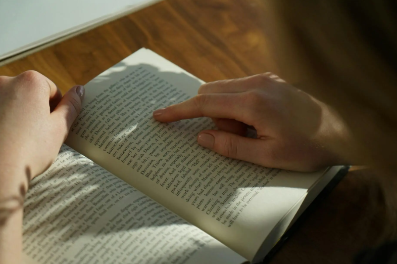 bir kitap üstünde parmağıyla takip yaparak okuma yapan bir kişi
