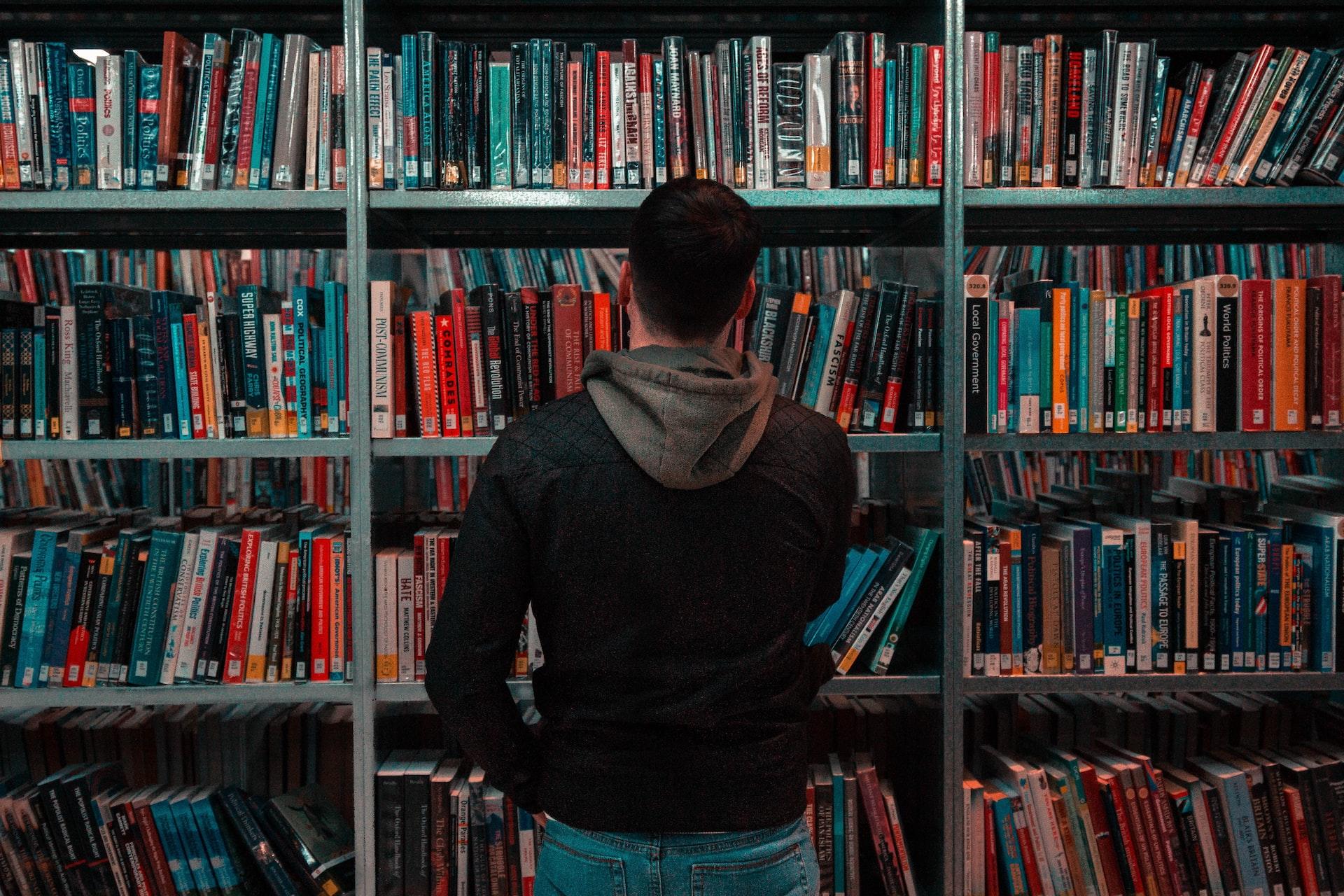 Хлопець дивиться на стелаж з книгами в бібліотеці