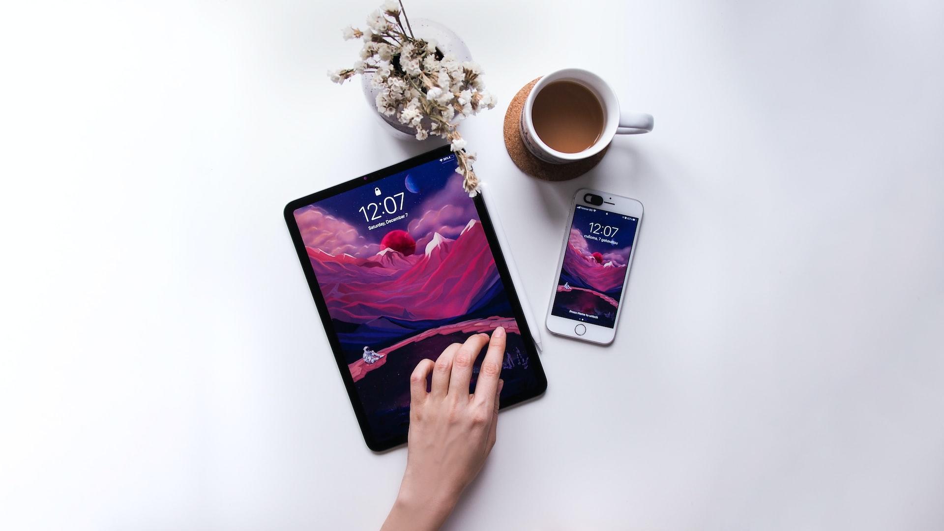 планшет та смартфон, чашка кави, кисть жінки на білому фоні