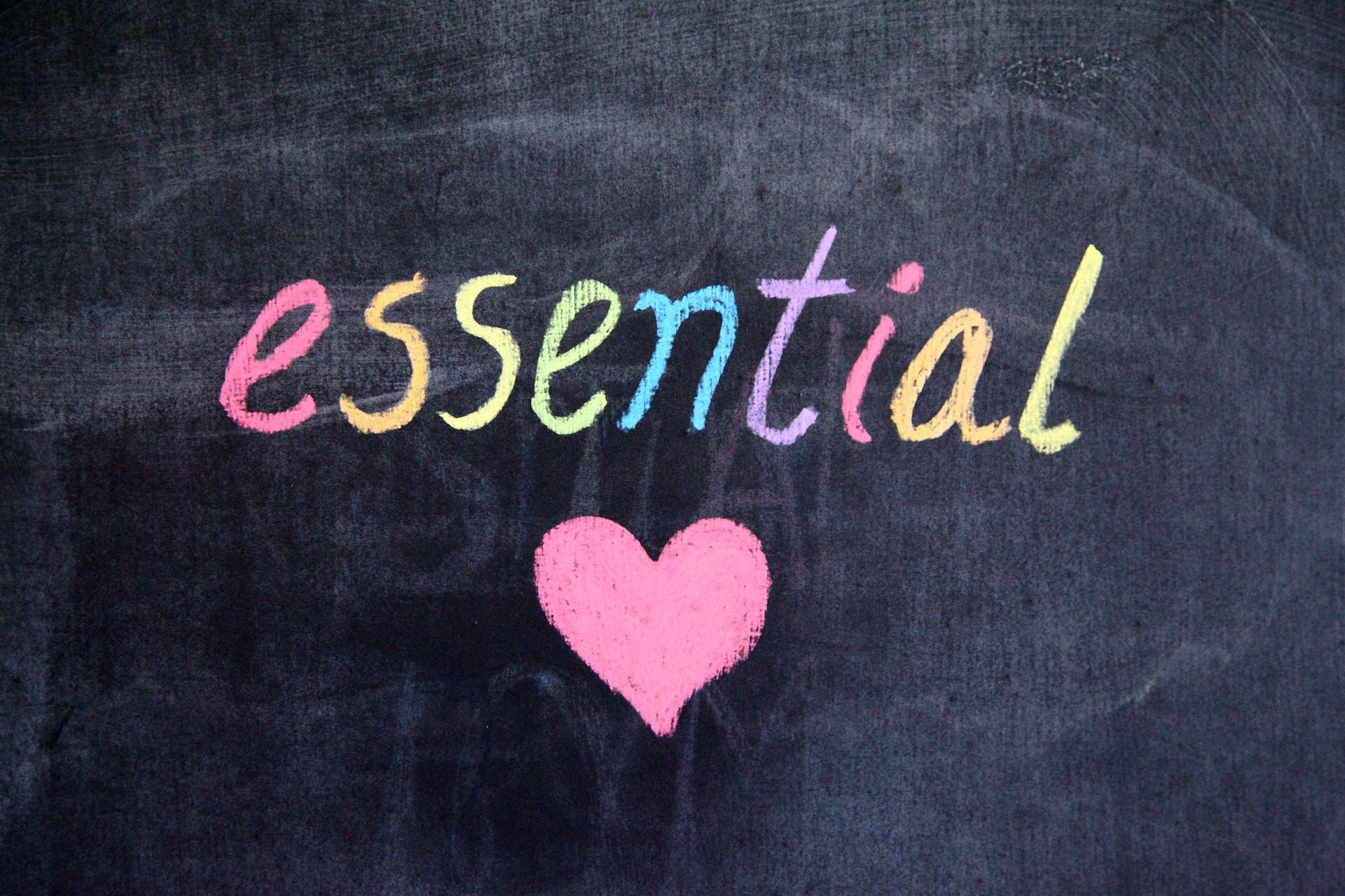напис "essential" кольоровою крейдою на чорній дошці з рожевим сердечком