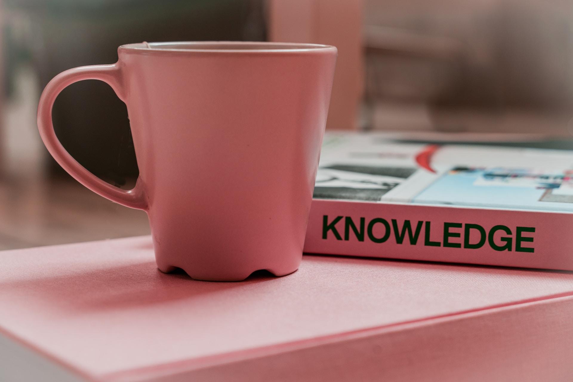 рожева чашка на рожевому столі з рожево. табличкою "knowledge"