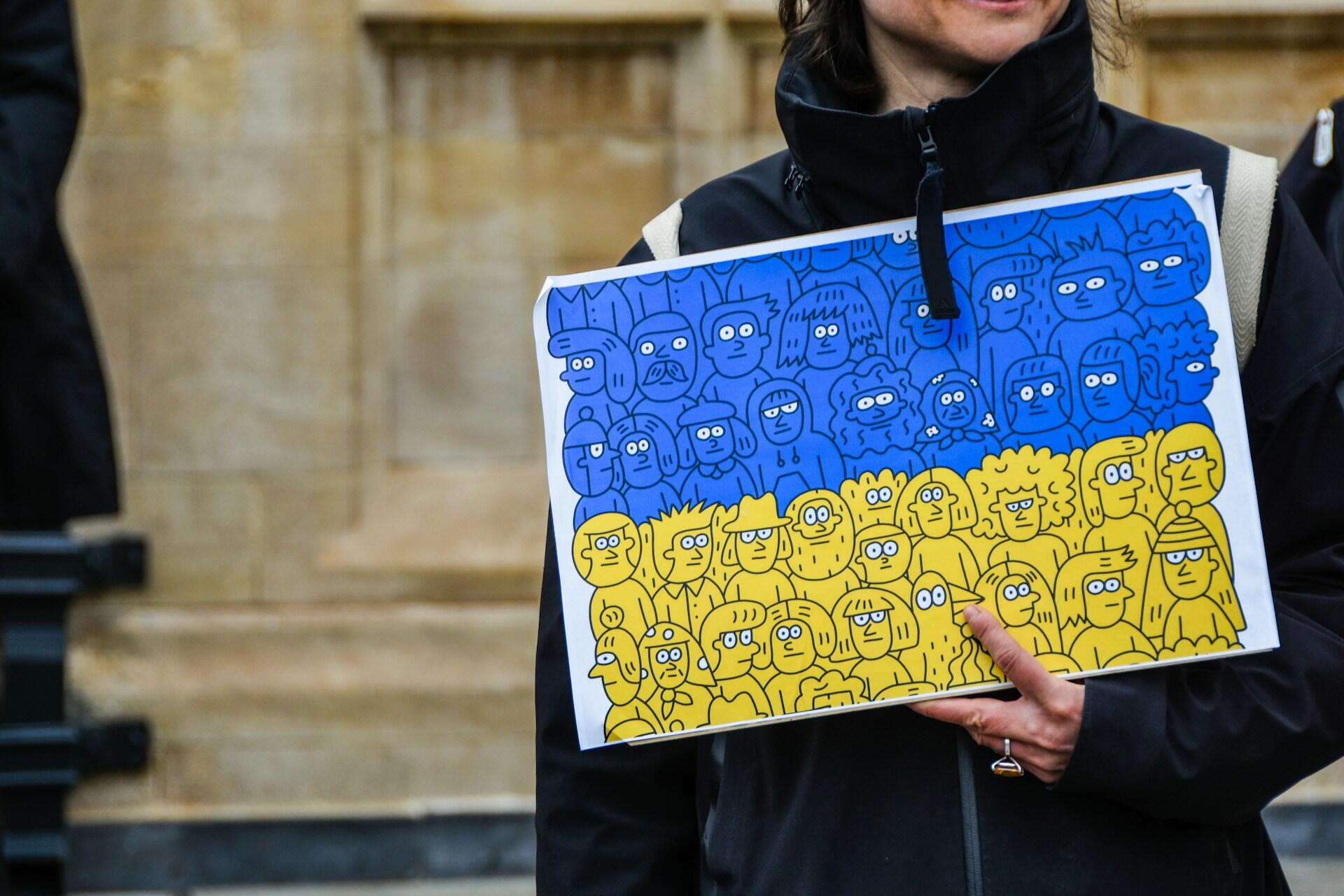 хлопець тримає малюнок, на якому схематично зображено людей, на синьо-жовтому фоні, що символізують українське суспільство