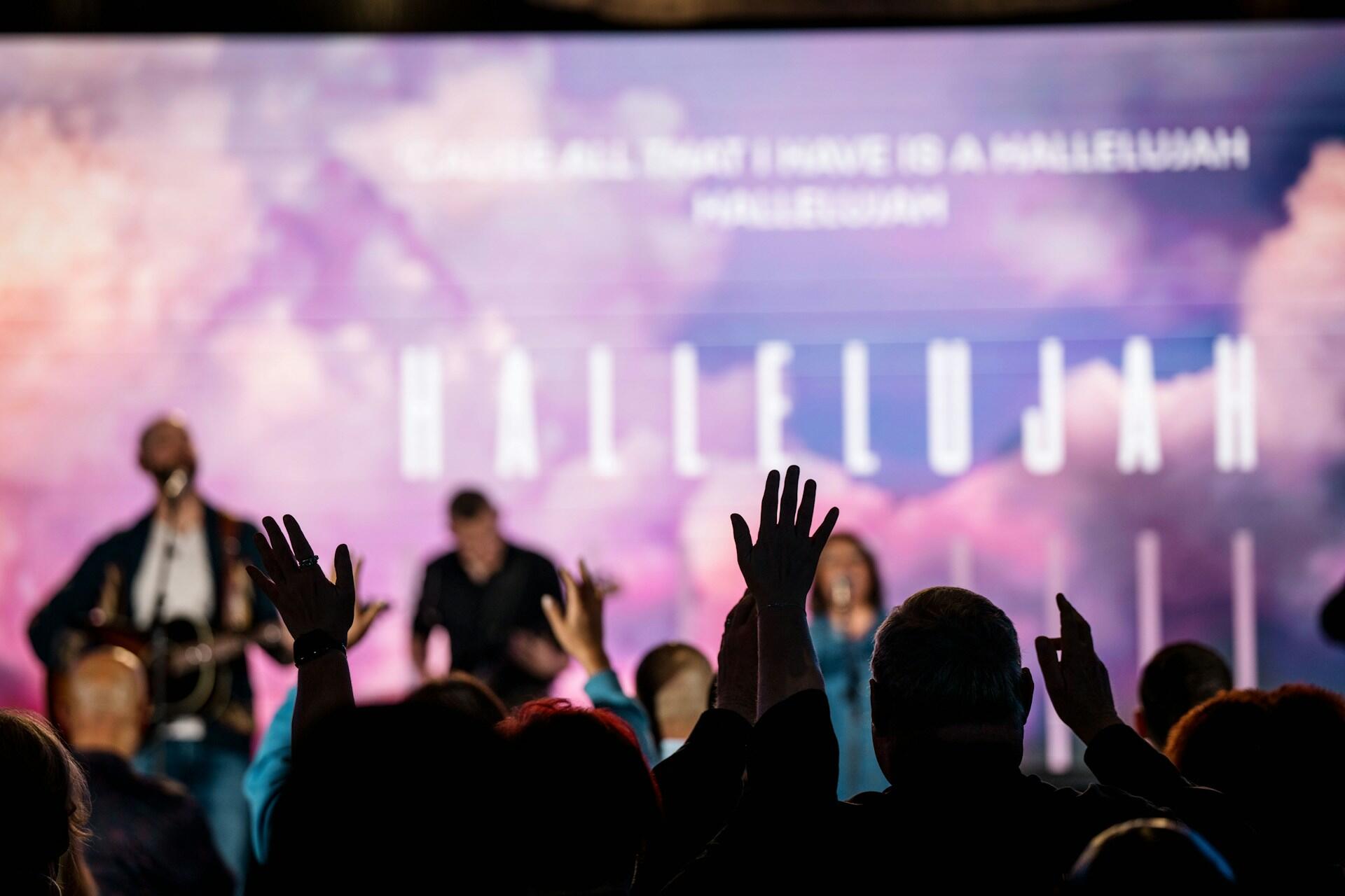 Музиканти на сцені на фоні заднику з написом Алілуя, на передньому плані натовп слухачів з піднятими руками