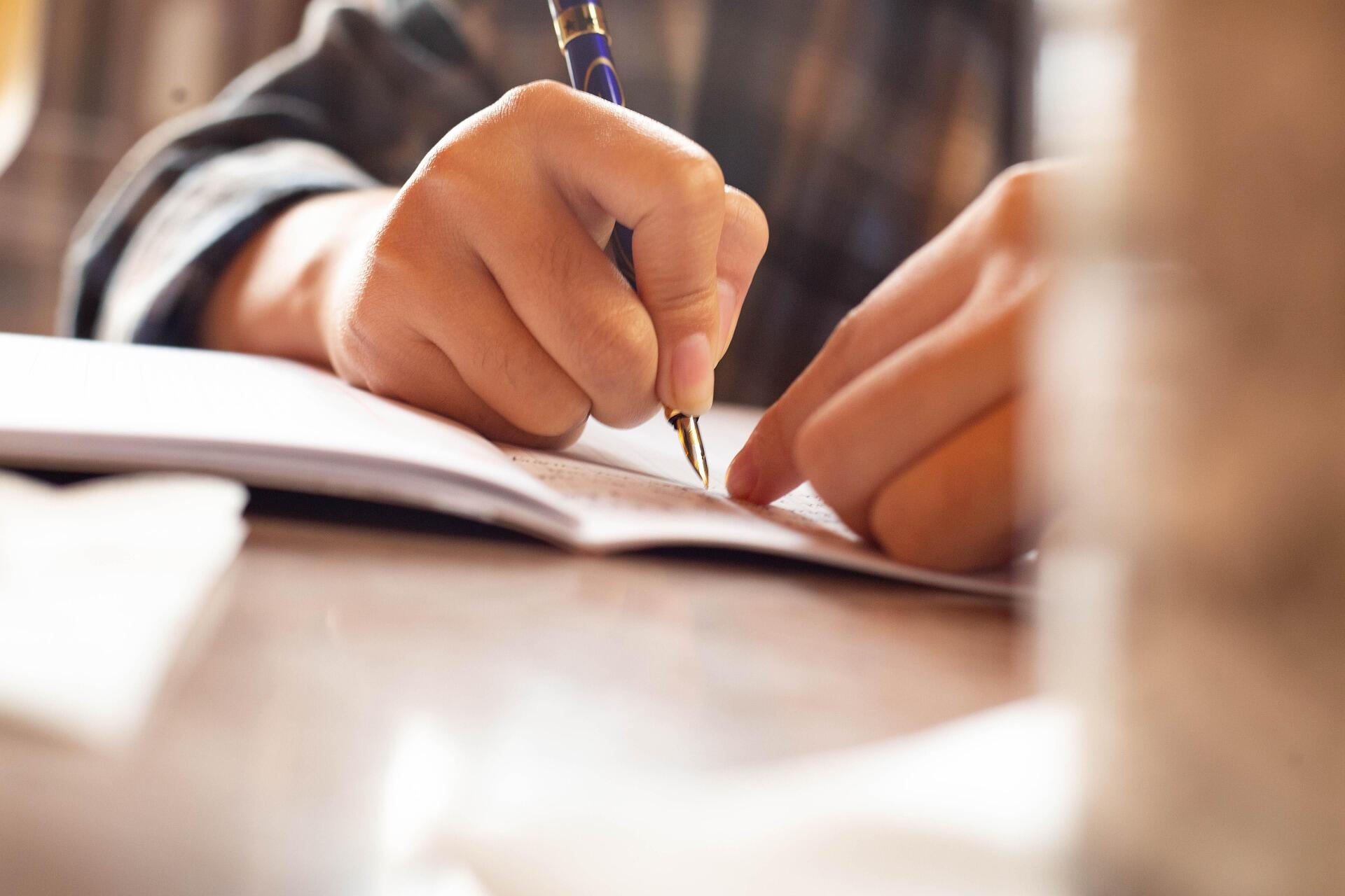 Макро зображення руки хлопця, що пише у зошиті
