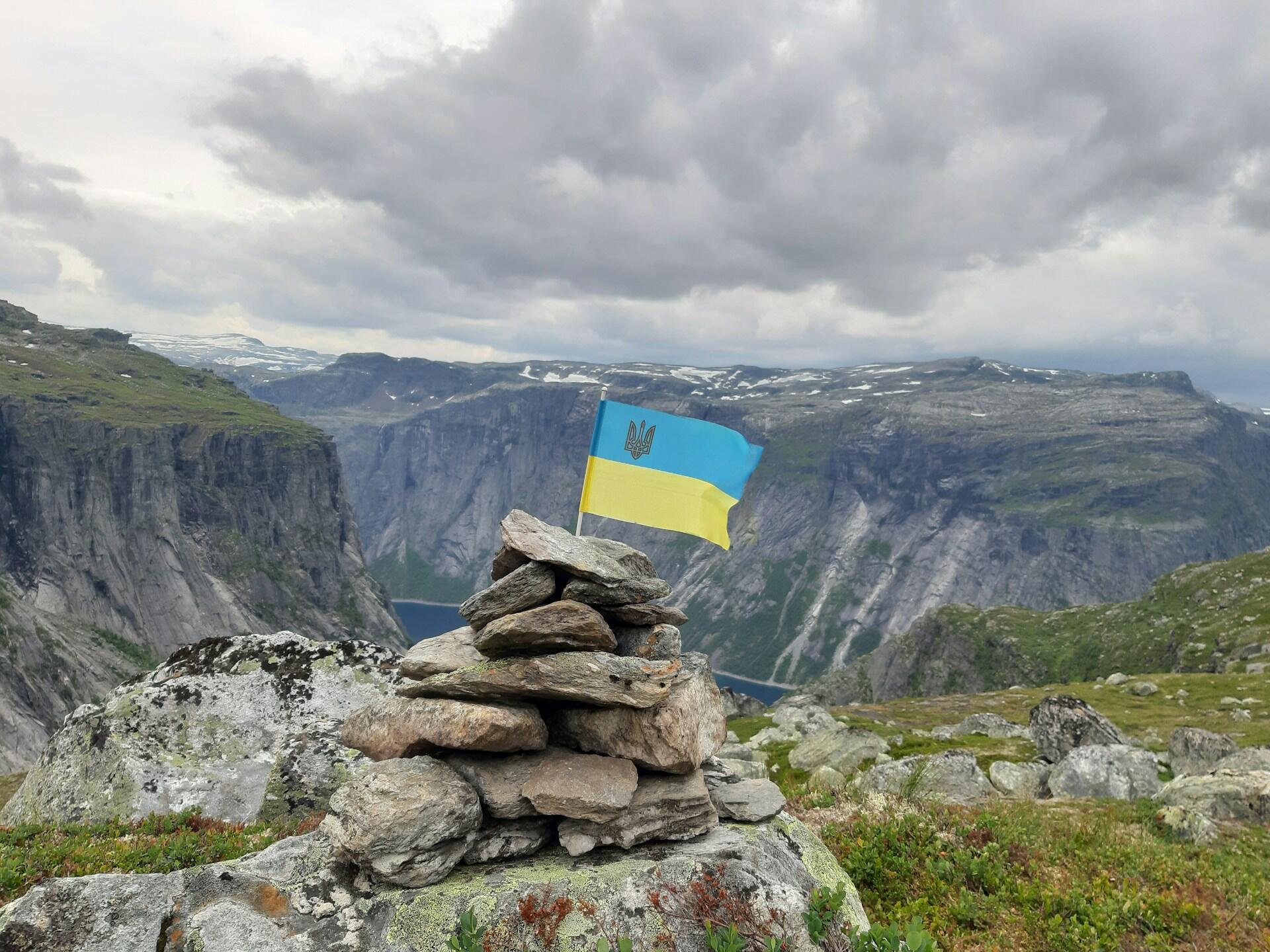 маленький прапор України встромлений у купку камінців на фоні норвезьких фйордів
