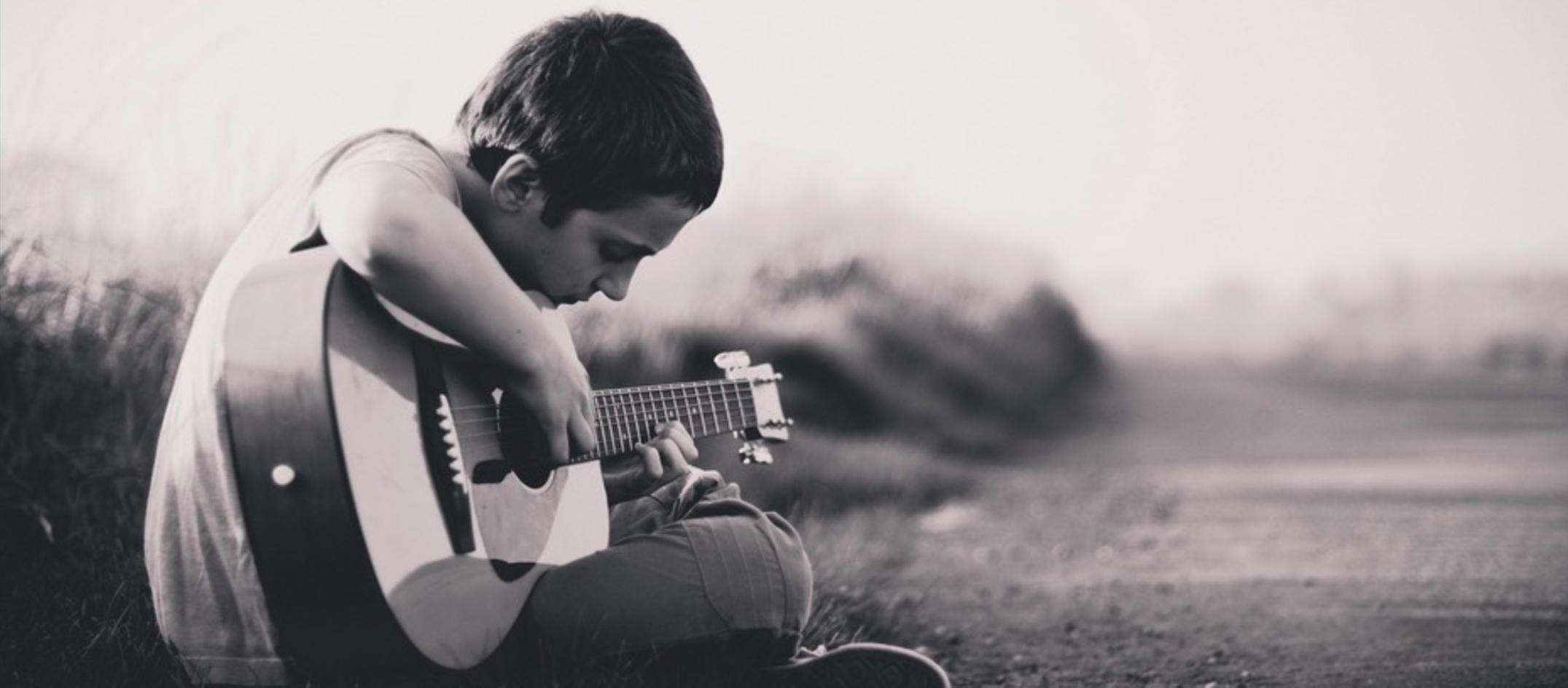 A young man learning the guitar outside.