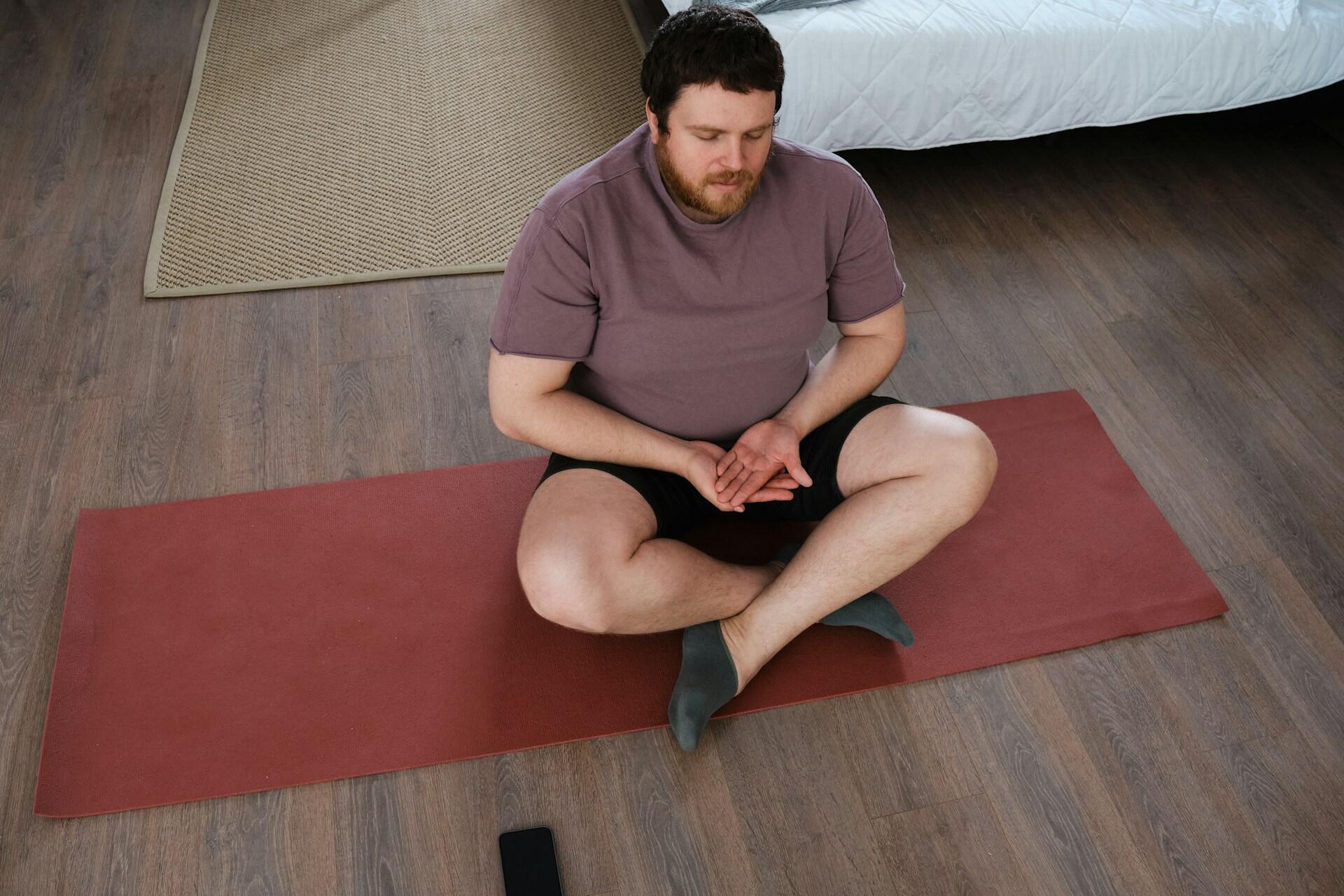 A man sitting criss crossed on a yoga mat.