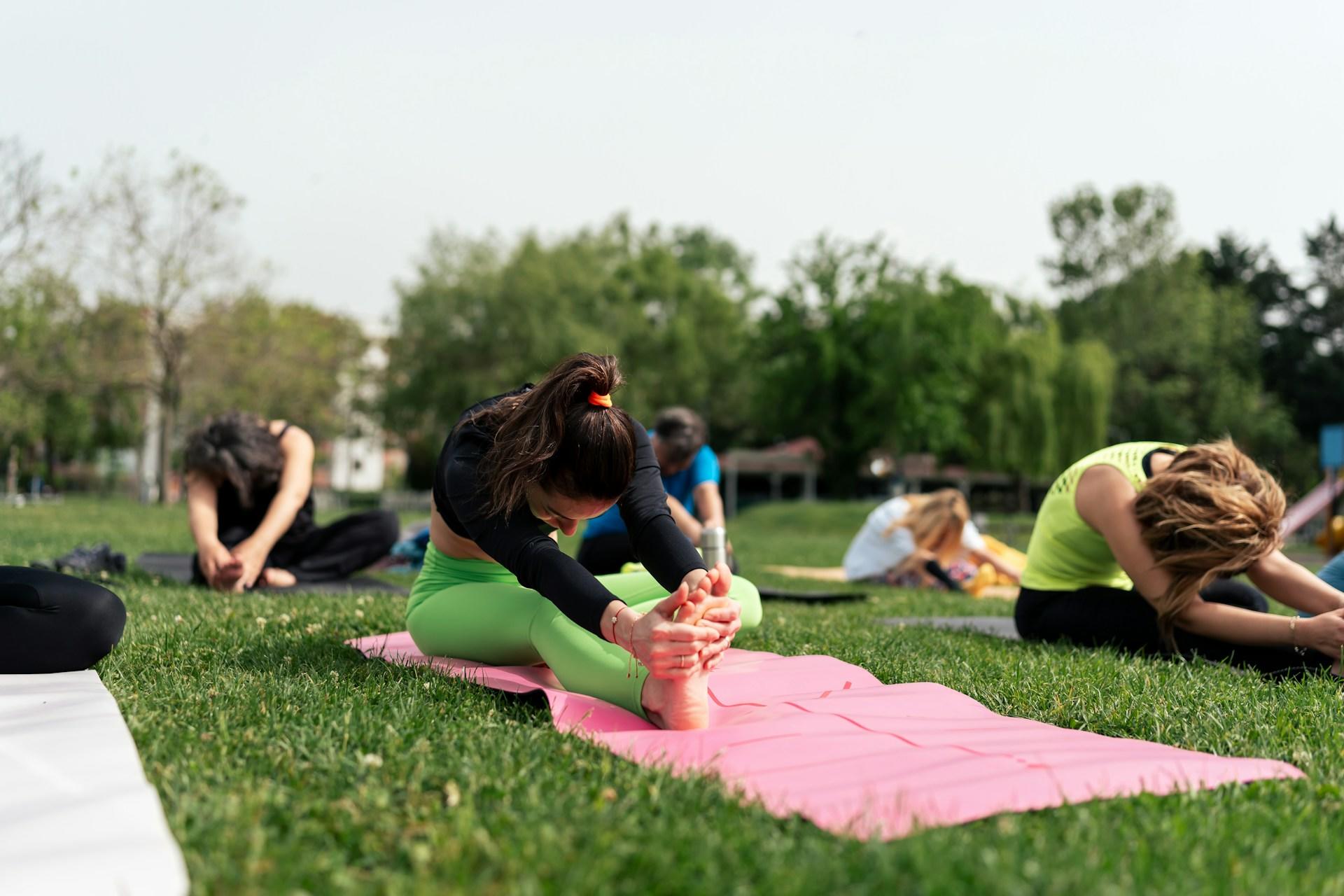 A yoga class in the park with participants stretching.