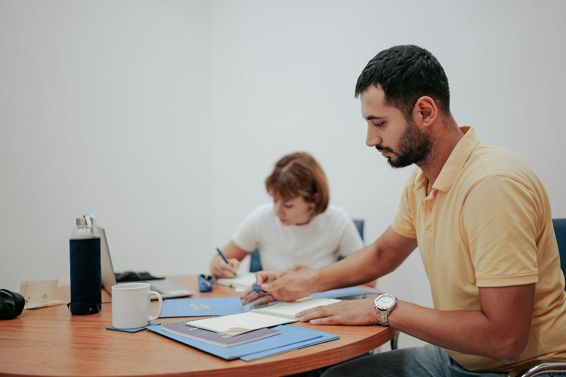 Two people writing in their notebooks during a tutoring session.