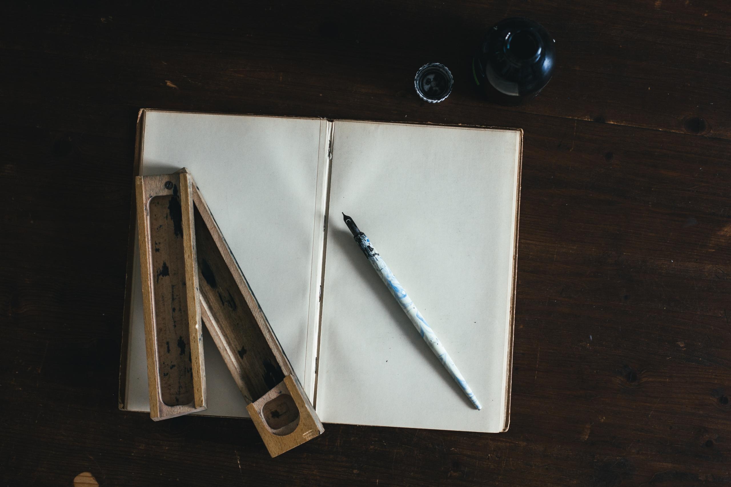 A white fountain pen and a white sketchbook are placed on the table