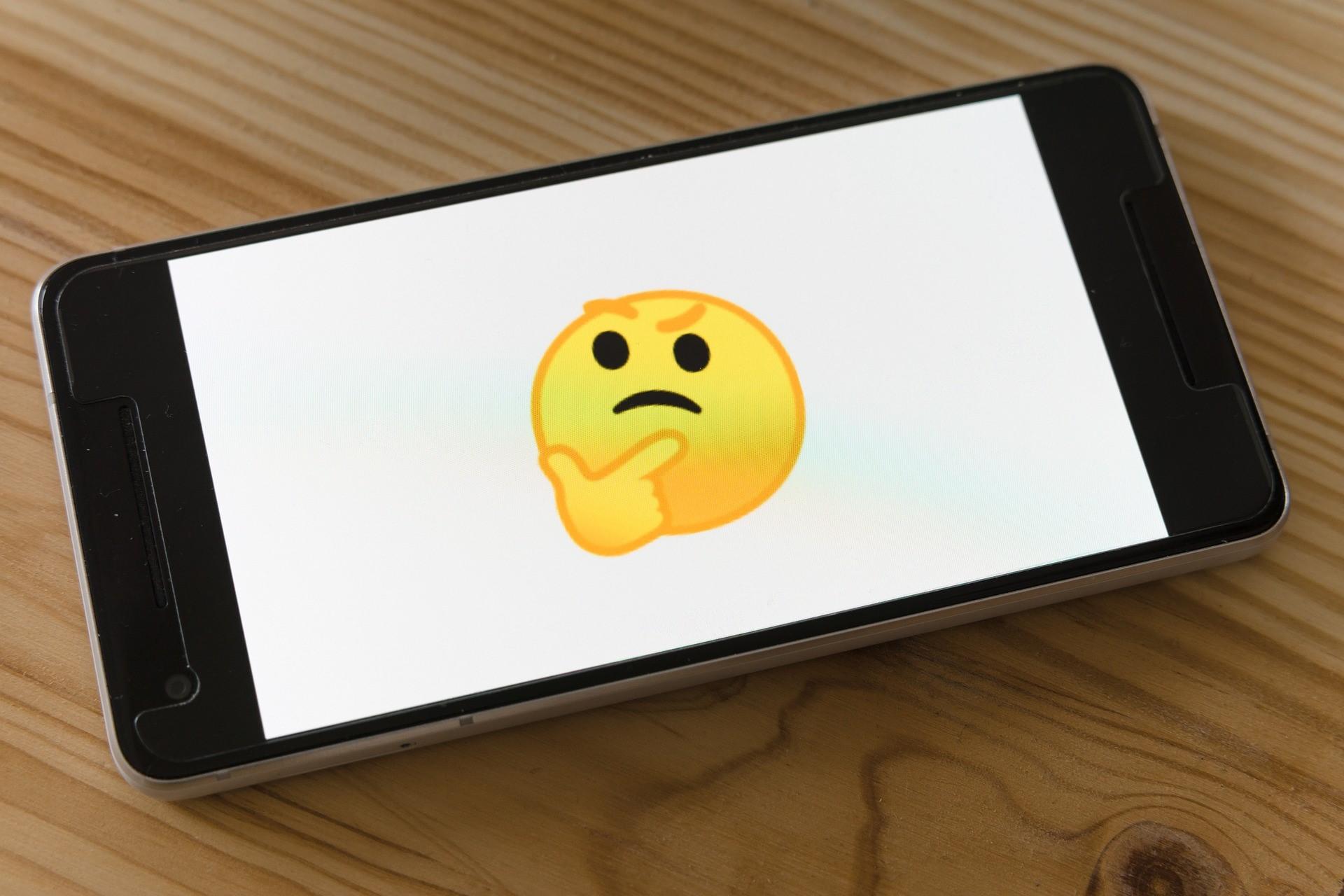 A thinking emoji is displayed on the phone. This fast world requires brief comments, and gone are the days where you need words to describe how you feel. A simple 'react' usually does the job, which negates some of the benefits of writing, such as avoiding miscommunication and wholesomely expressing your feelings