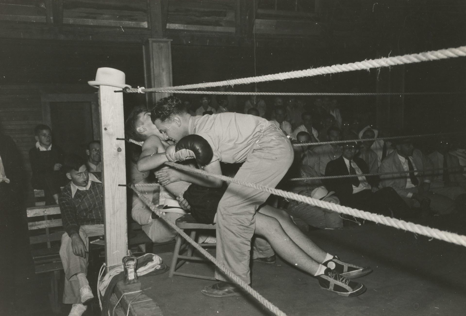 Two boys in the boxing ring with spectators around the ring.