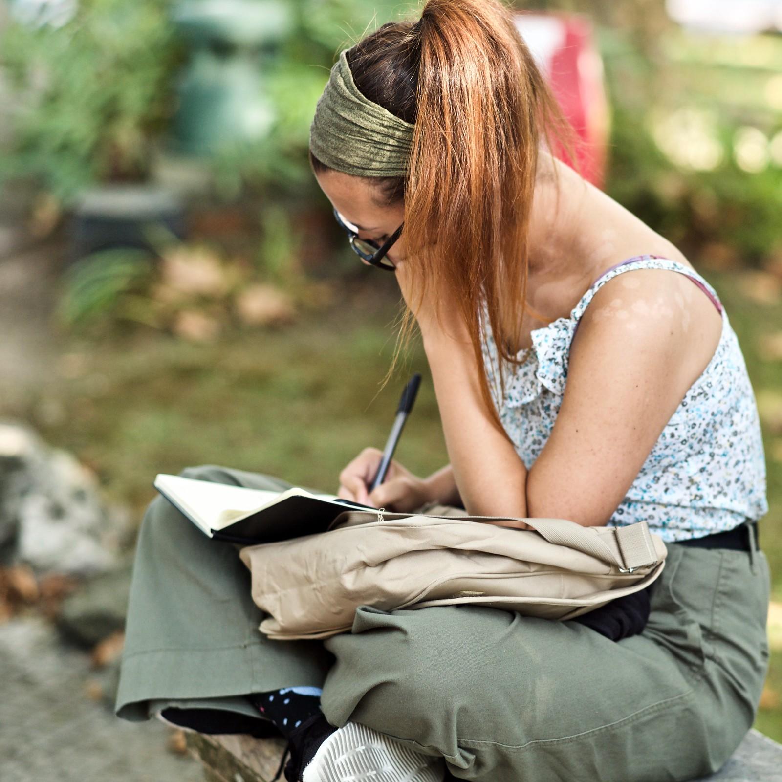 A woman sitting on the bench and writing in a notebook. The best way to strengthen your English writing skills is by practicing every day, whether you choose to journal, write stories, or create internet posts