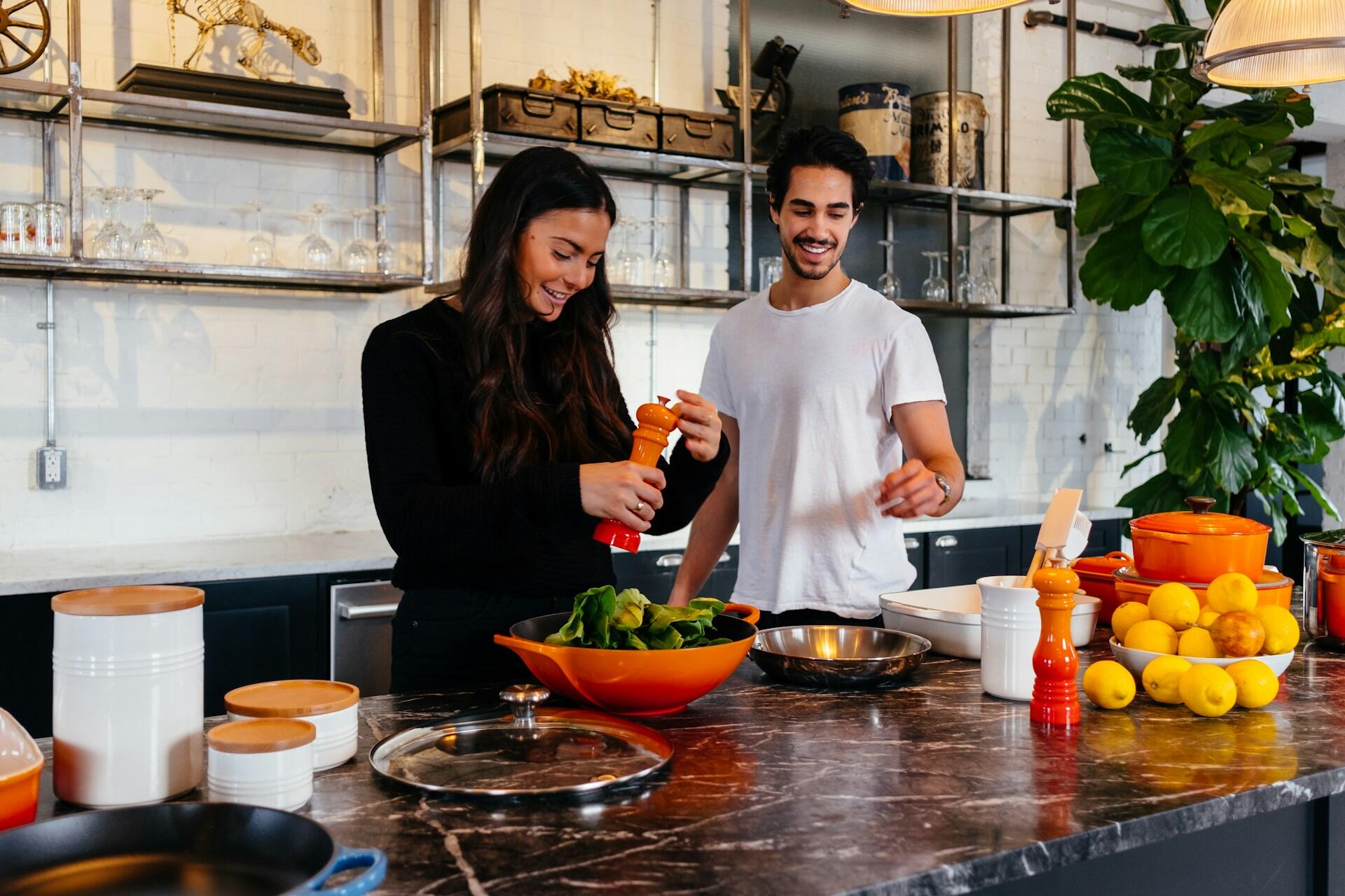 A couple cooking together in the kitchen by putting salt on vegetables.