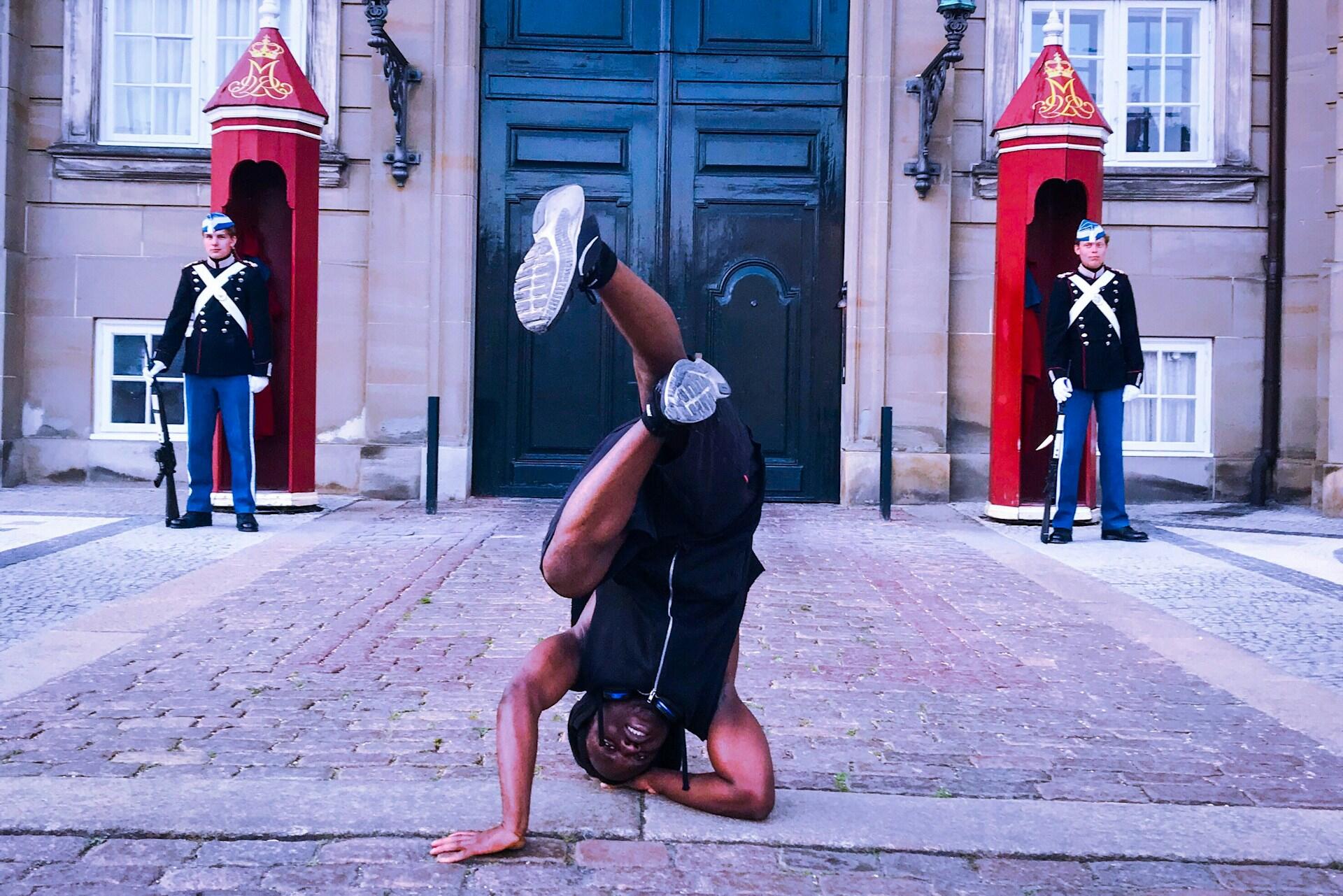 A man break dancing in front of a palace with guards.