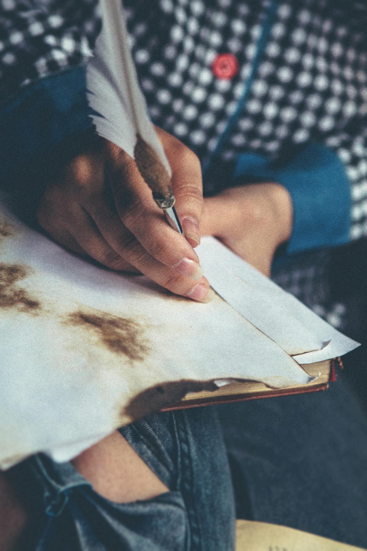 person using a quill pen to write on a rustic piece of paper