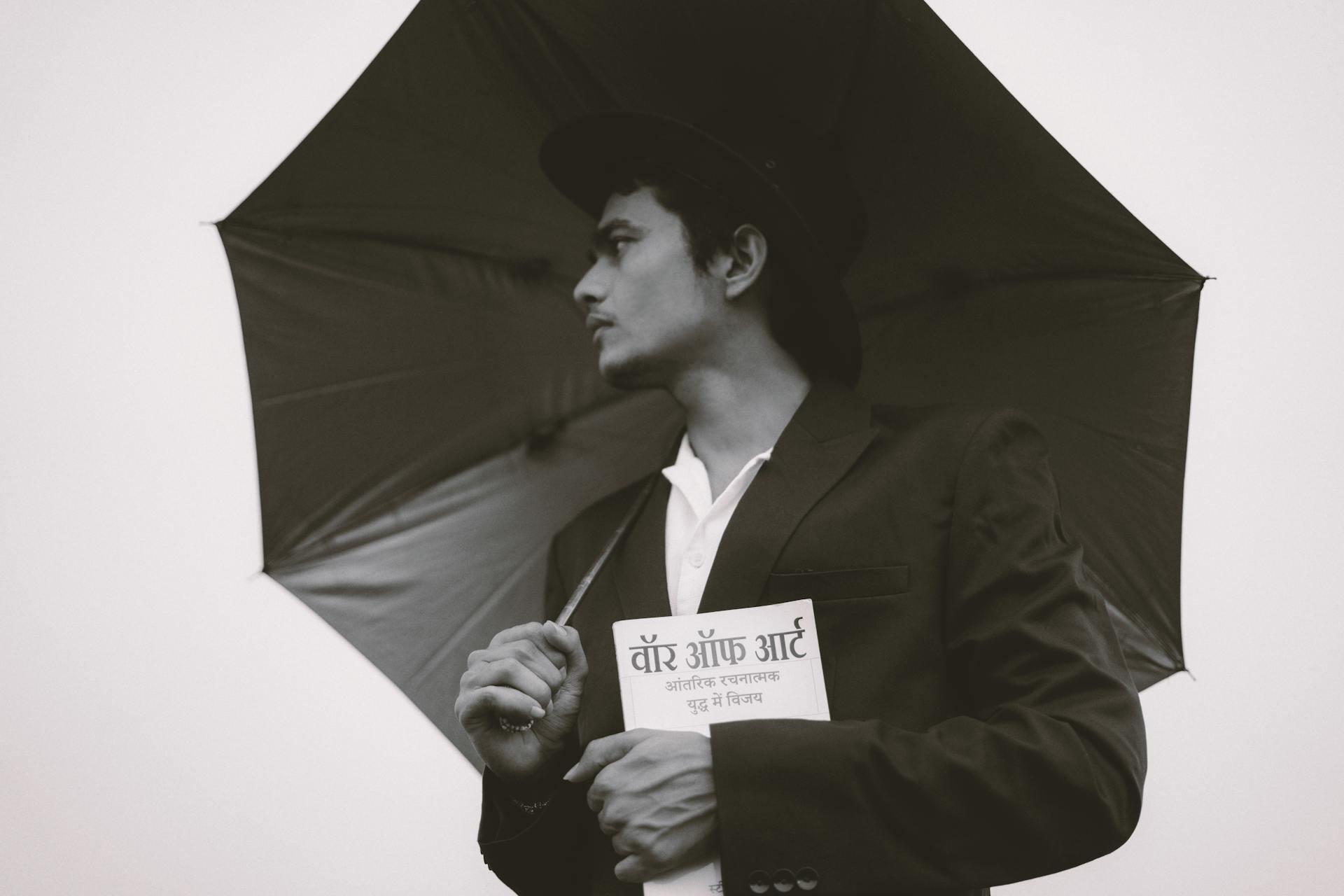 a black and white photo of a man holding a book written in Hindi in one and and an umbrella in the other hand