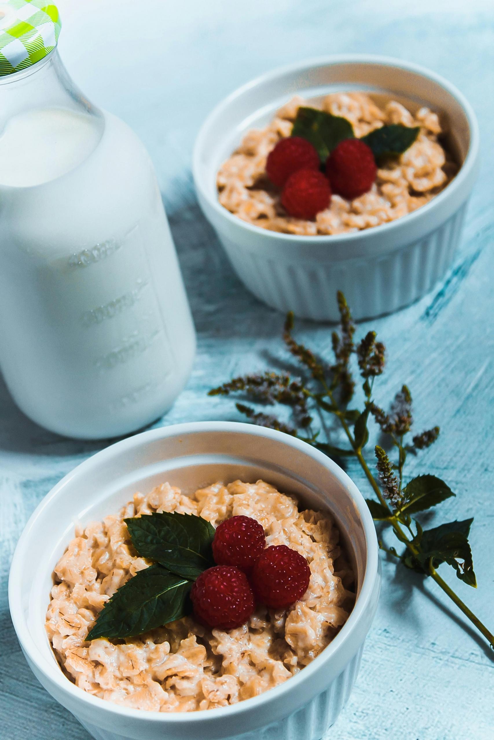 Two bowls of oatmeal and a bottle of milk on a table.