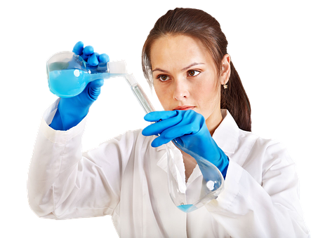 A woman wearing a laboratory coat transferring a blue chemical from one container to another