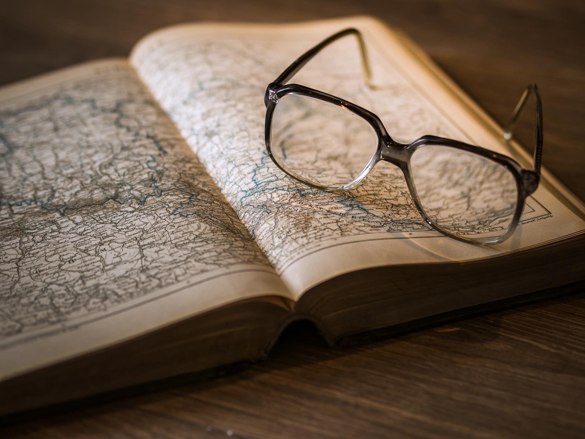 Glasses resting atop a book of maps. Studying history is filled with how civilizations changed the maps of the world