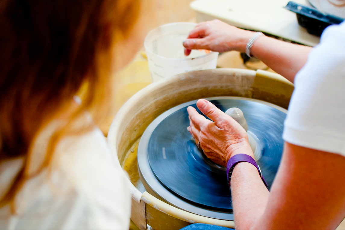 person sitting next to pottery wheel working on a piece.